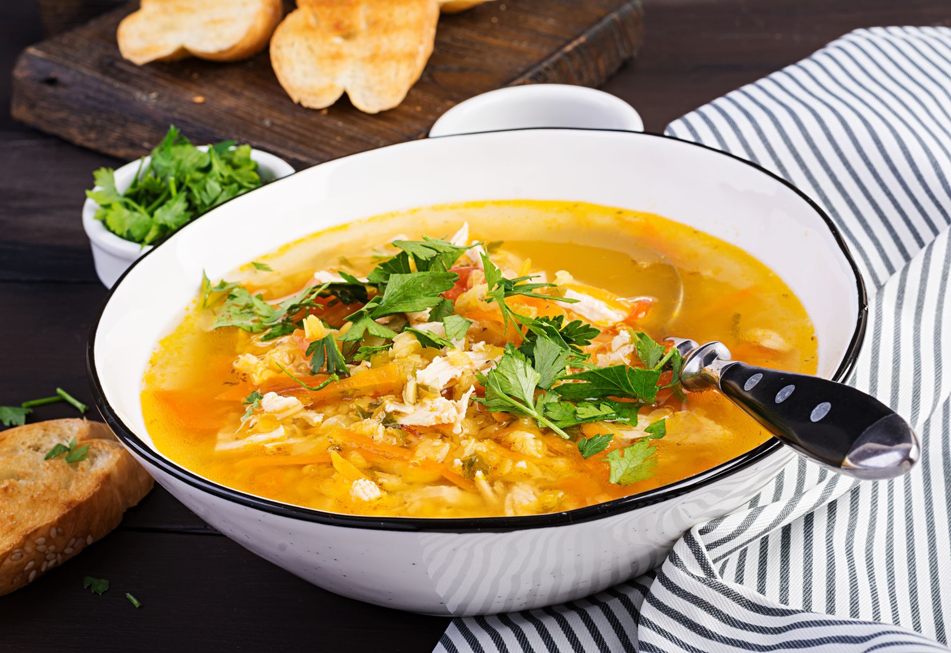 A bowl of golden soup topped with parsley, served with toasted bread on a dark wooden table.