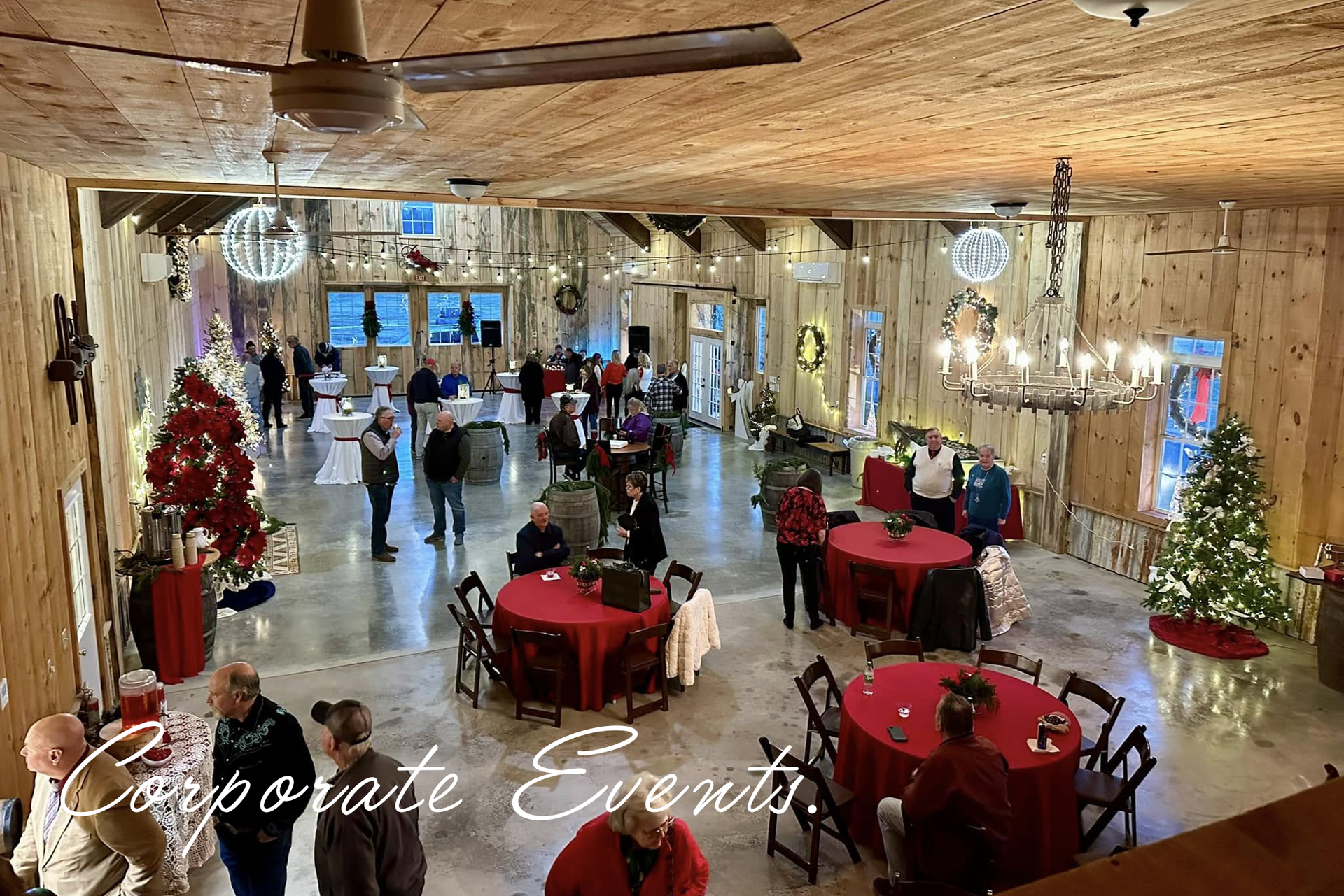 Event space with people mingling, red tables, holiday decorations, and a wood ceiling.