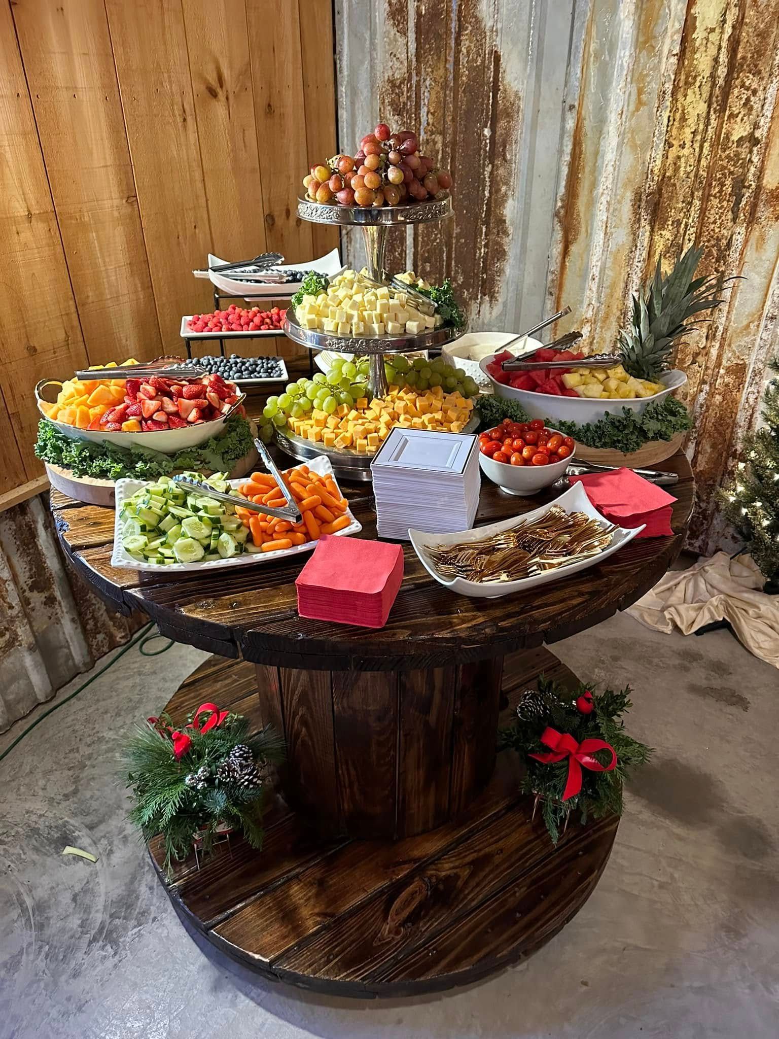 A round table made from a wooden cable spool displaying a buffet of colorful fruits and vegetables.