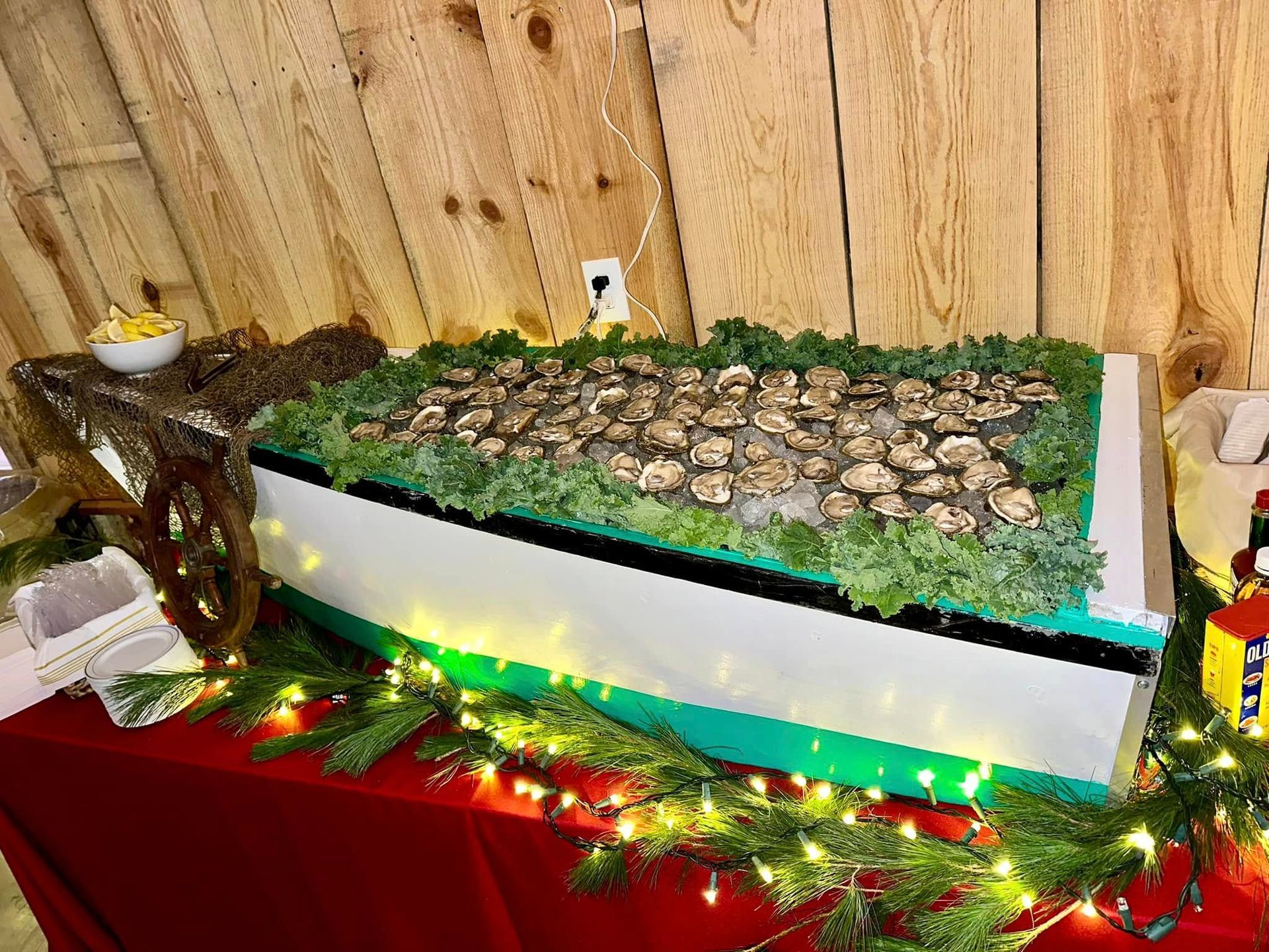 Oysters on ice arranged in a decorated boat on a table, festive greenery, and fairy lights.