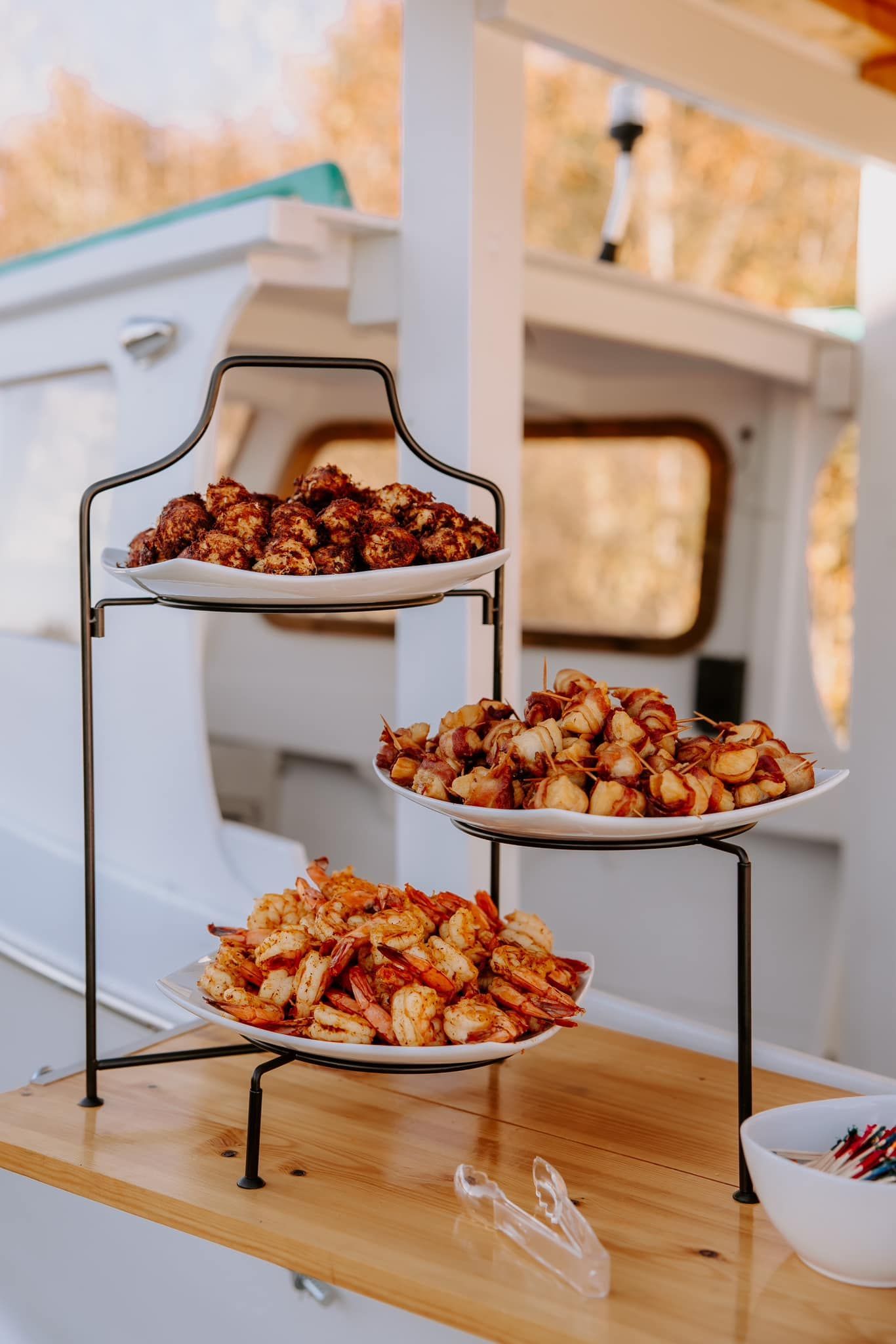 Three-tiered food display on a boat, featuring appetizers.