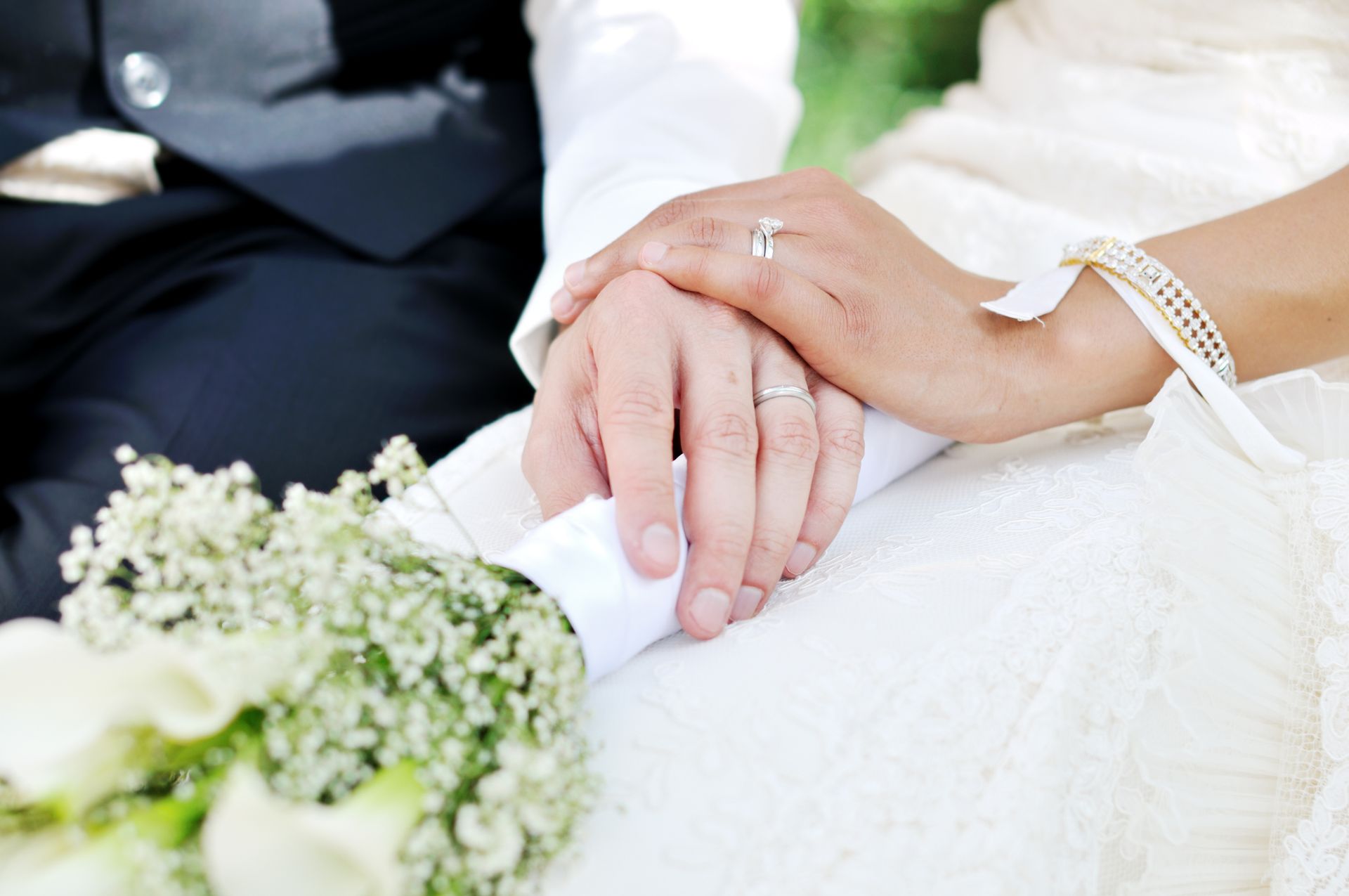 Una sposa e uno sposo si tengono per mano mentre sono seduti accanto a un mazzo di fiori.