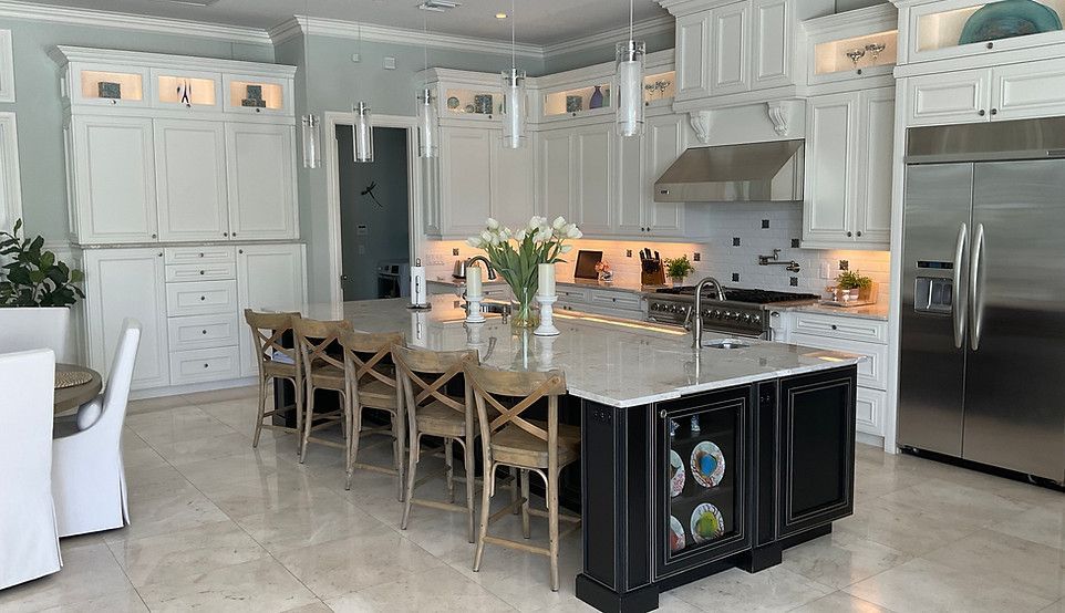 Bright white kitchen with granite island, stainless refrigerator, and open view into a living area
