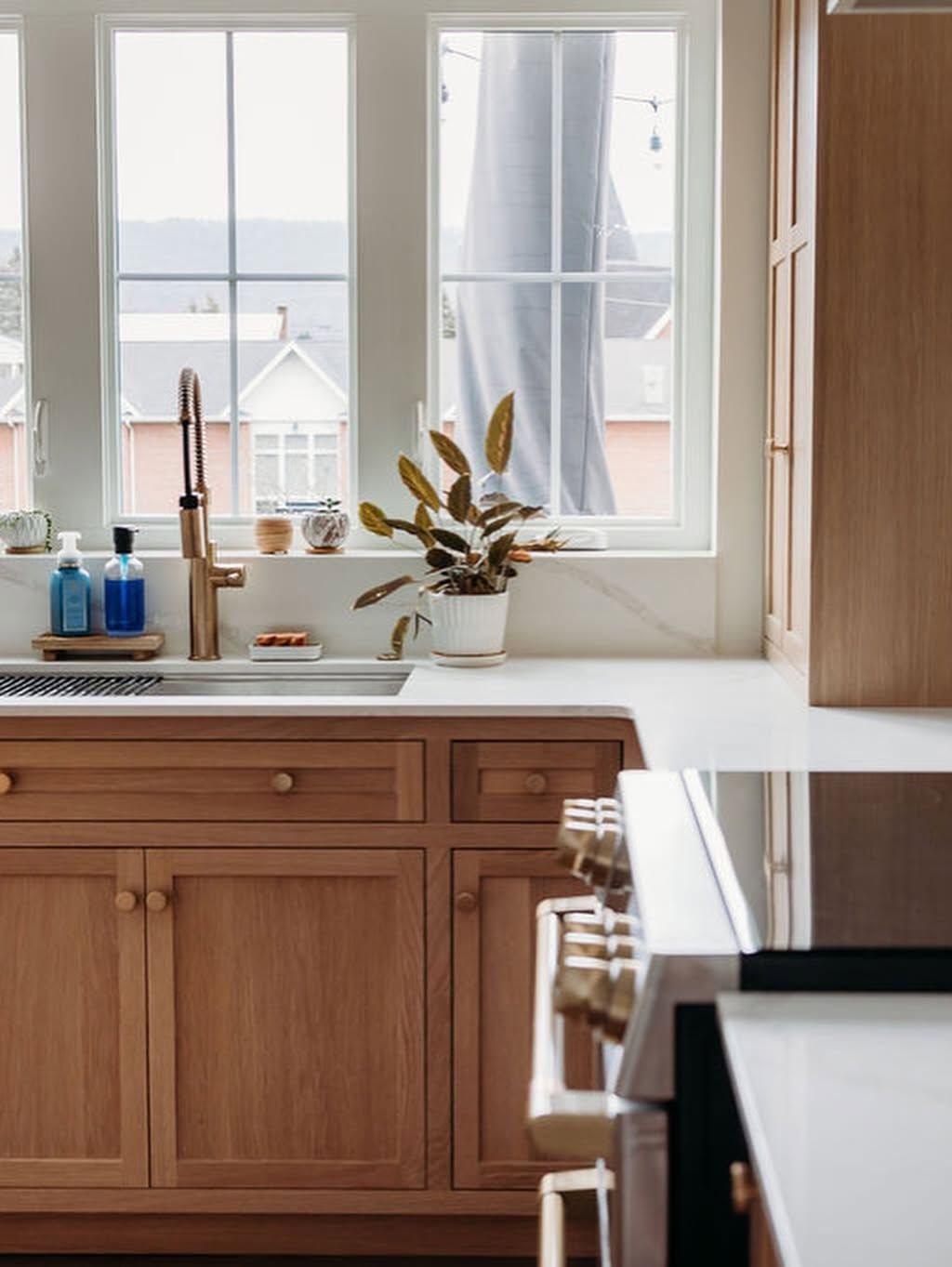 Bright kitchen with wood cabinets, white countertops, and a potted plant by two windows.