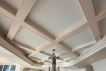 Coffered white ceiling with beige trim and a central chandelier in a bright room