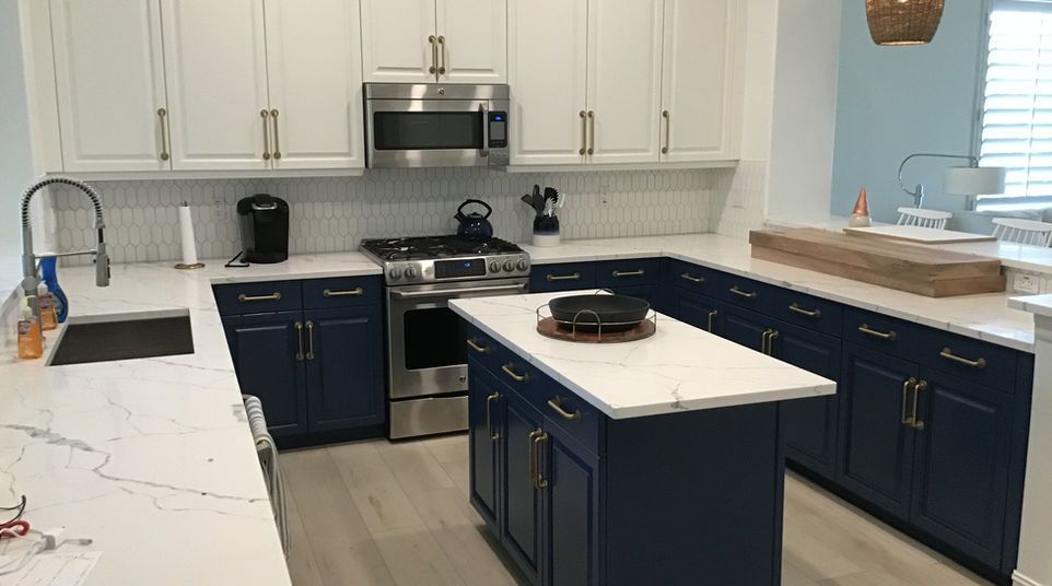 Modern kitchen with navy cabinets, white countertops, stainless appliances, and a central island.