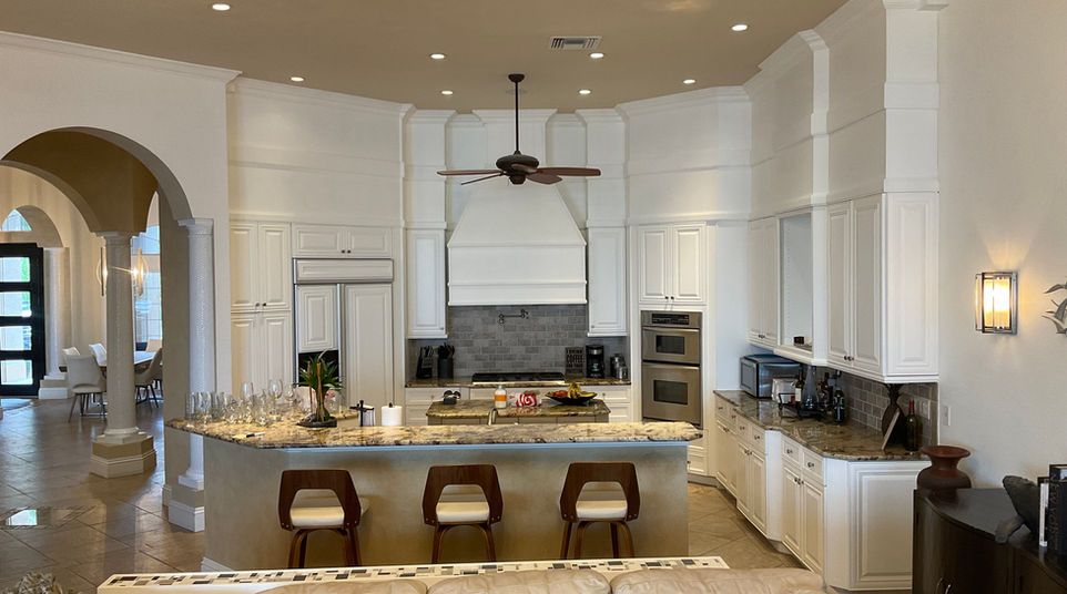 Bright modern kitchen with white cabinets, granite island, and barstools; arched doorway to hallway.