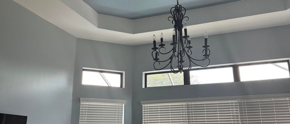 Gray room corner with a black chandelier and windows above white blinds.