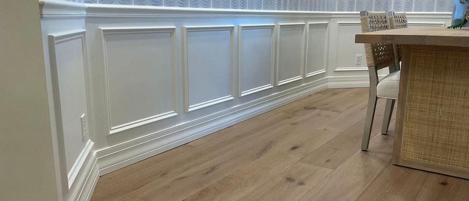 White paneled wall with wood flooring and a woven chair beside a table