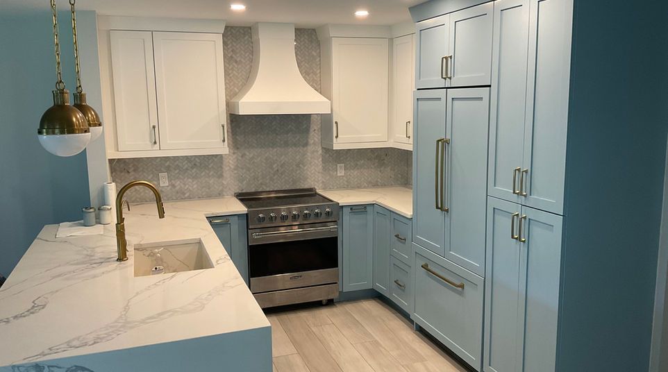 Bright blue kitchen with white cabinets, marble island, stainless stove, and brass pendant light