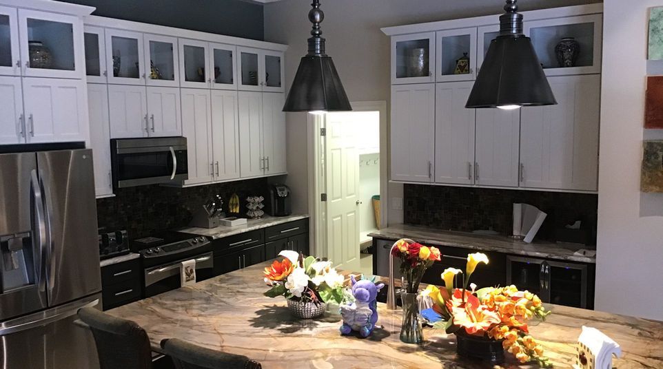 Bright white kitchen with granite island, stainless refrigerator, and open view into a living area