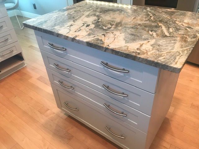 White kitchen island with marble-look countertop and four drawers on a wooden floor