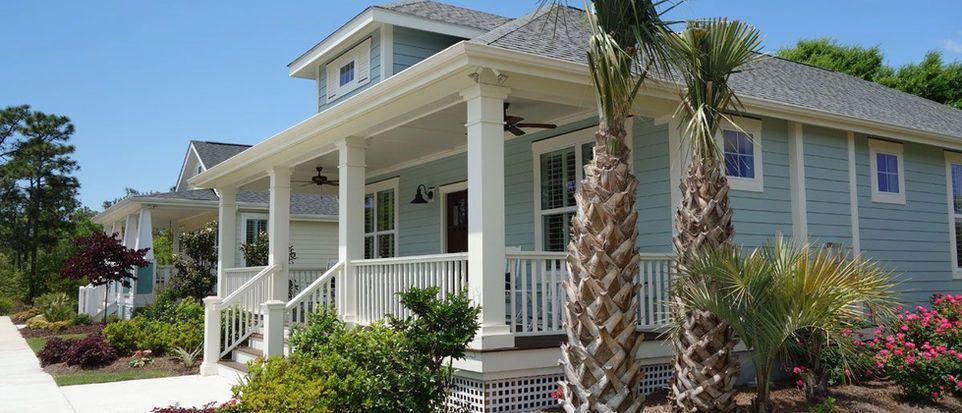 Beach house with white porch, gray siding, and palm trees in a sunny coastal setting