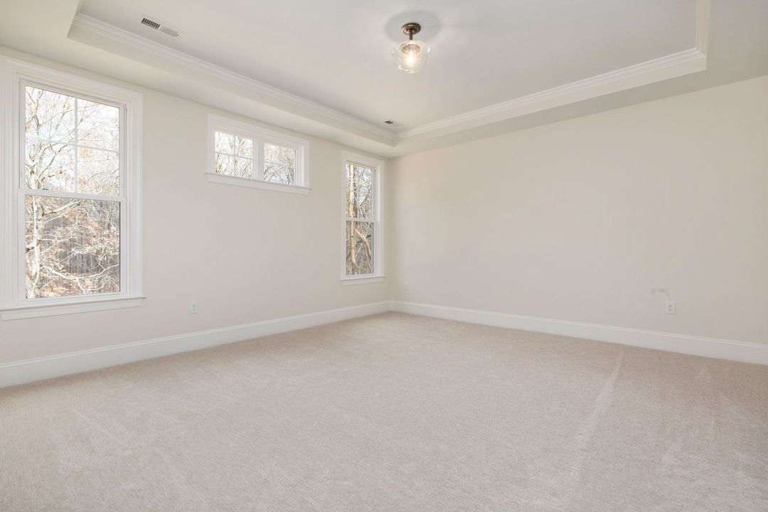 Empty beige bedroom with white trim, carpeted floor, and three windows letting in daylight