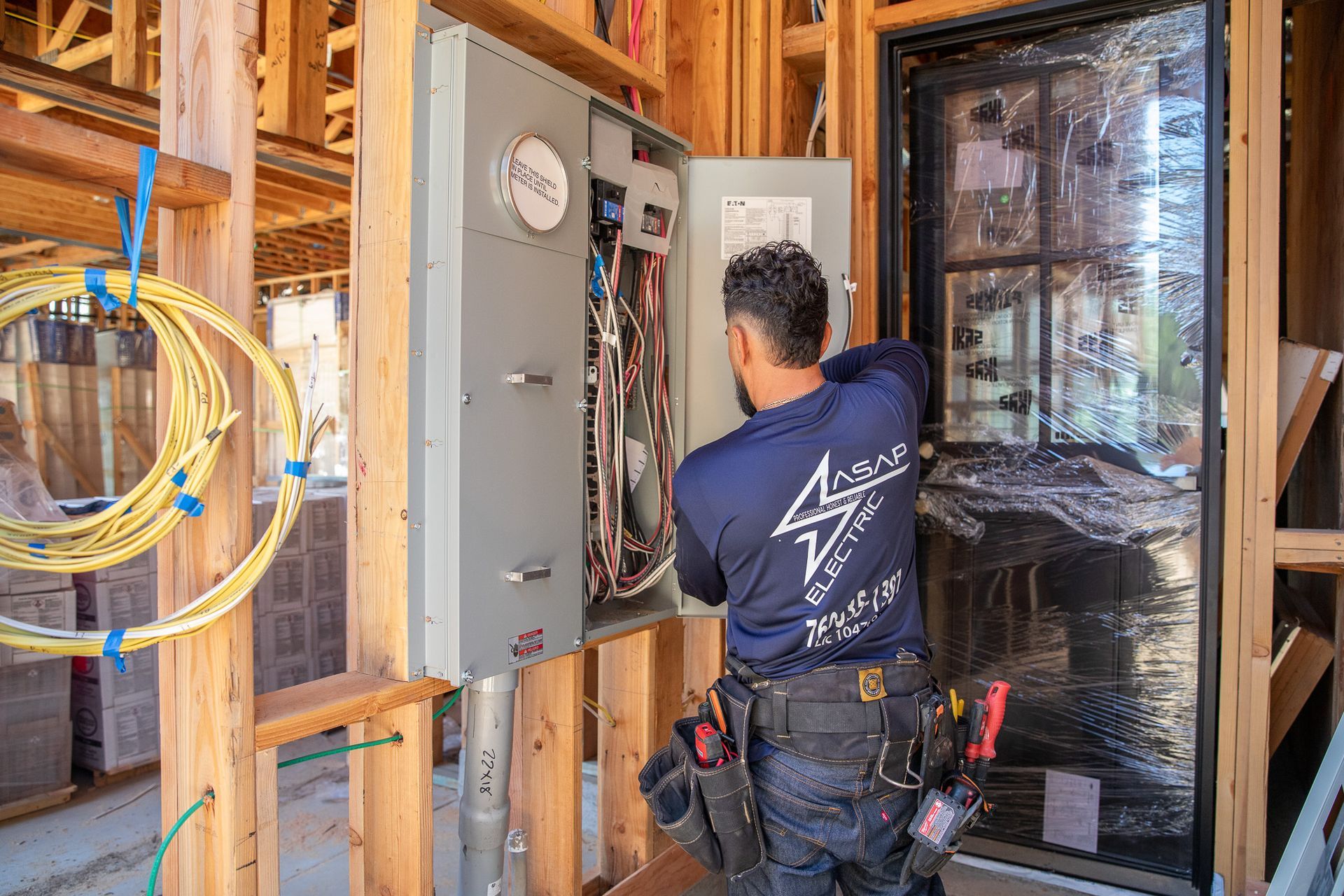 Electrician working on an open electrical panel inside a framed construction site