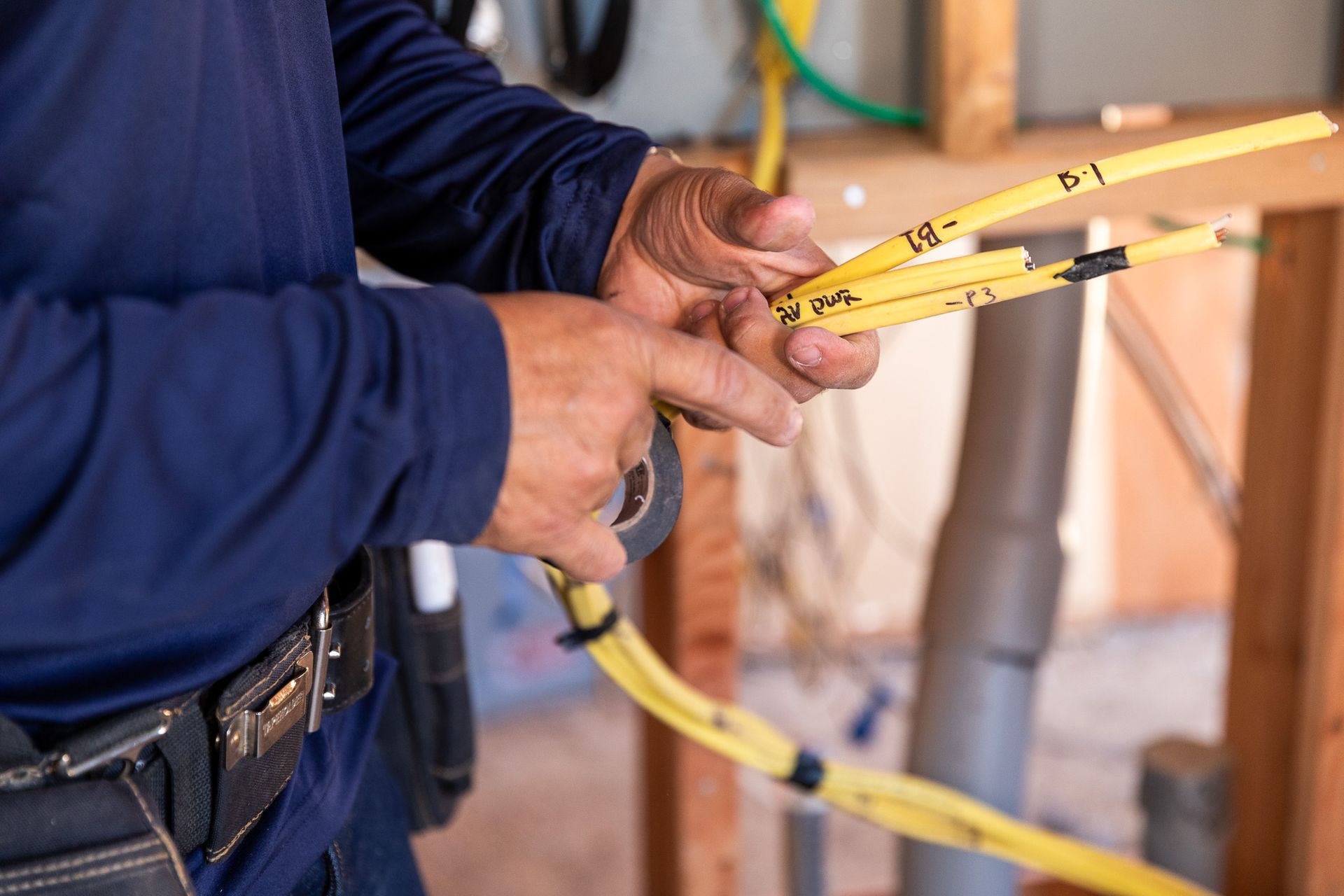 Electrician with yellow wires, standing in wooden frame of a house.