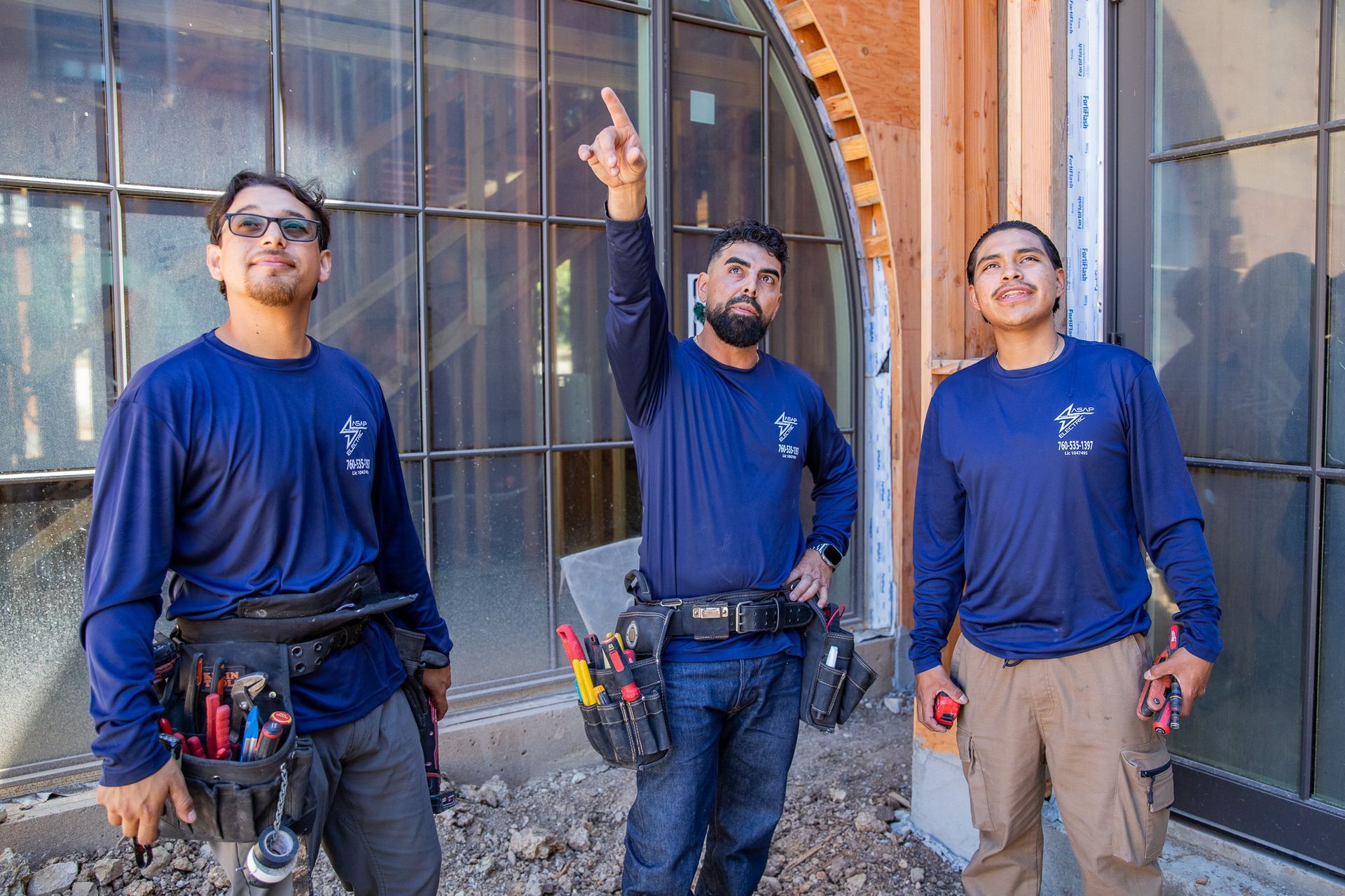 Three workers in blue shirts standing outside a building, one pointing upward.