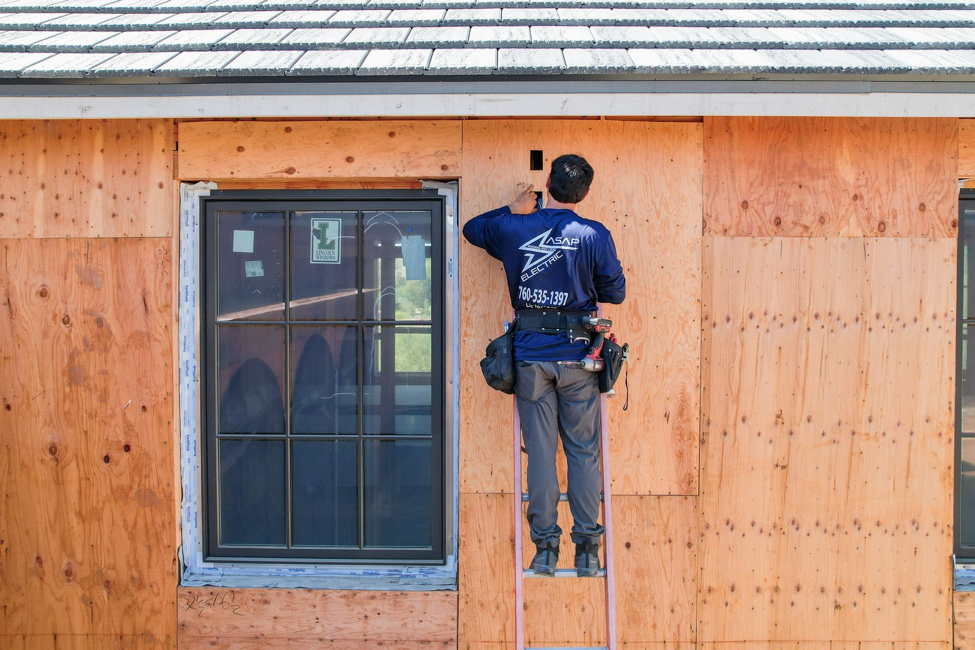 Worker installing siding on a house exterior beside a window