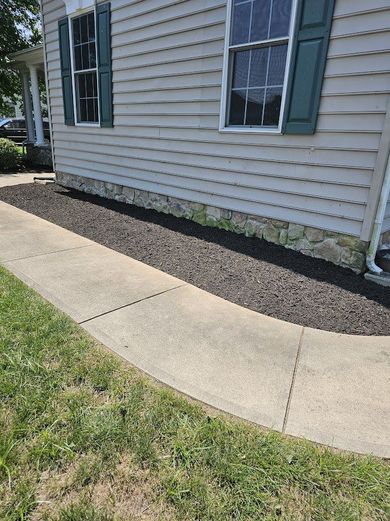 Curved concrete walkway beside a beige house with white siding, green shutters, and a mulch strip along the foundation Curved concrete walkway beside a beige house with white siding, green shutters, and a mulch strip along the foundation