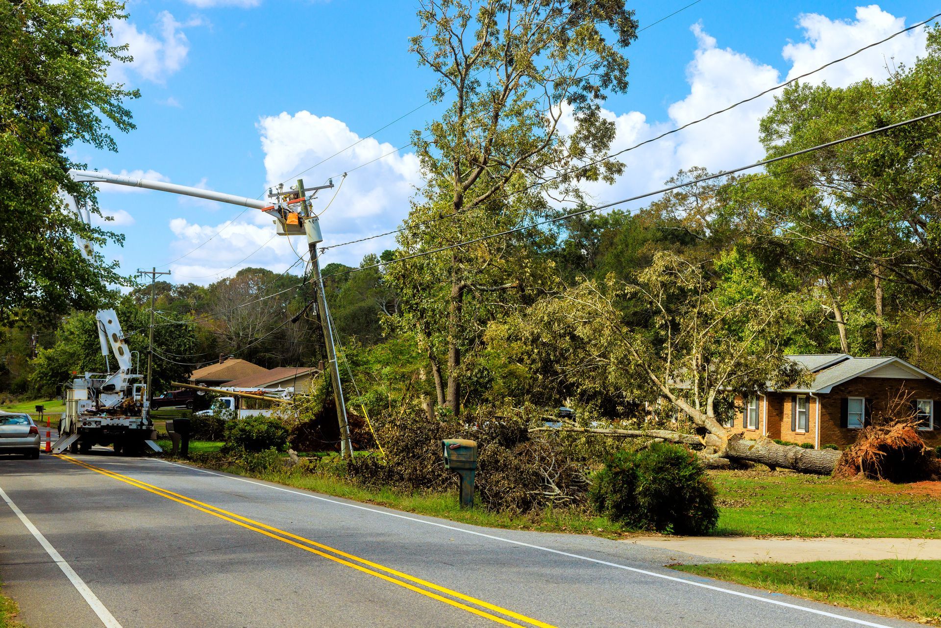 Quiet rural road with power lines, trees, and houses under a bright blue sky