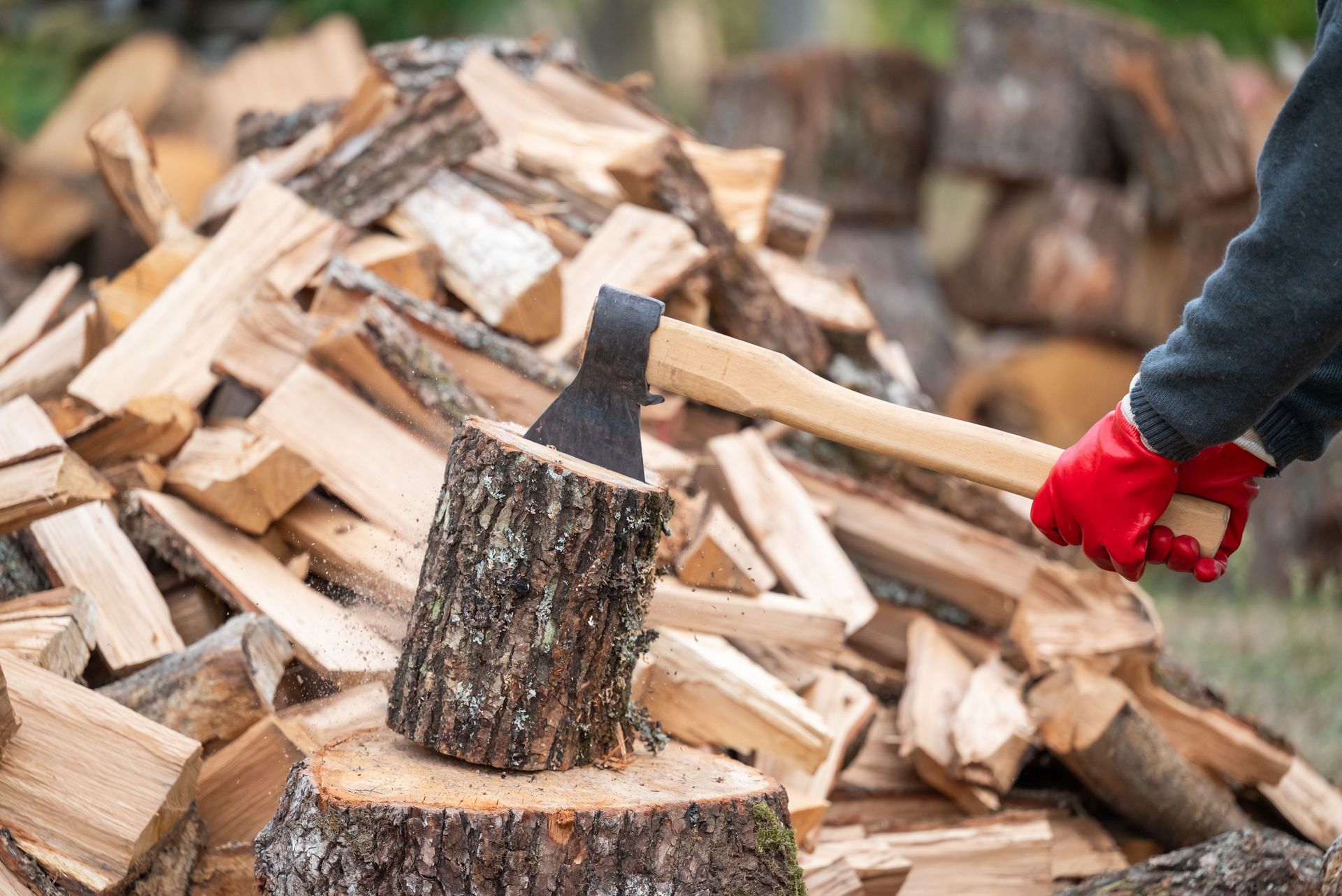 Gloved hand chopping firewood beside a split log pile outdoors