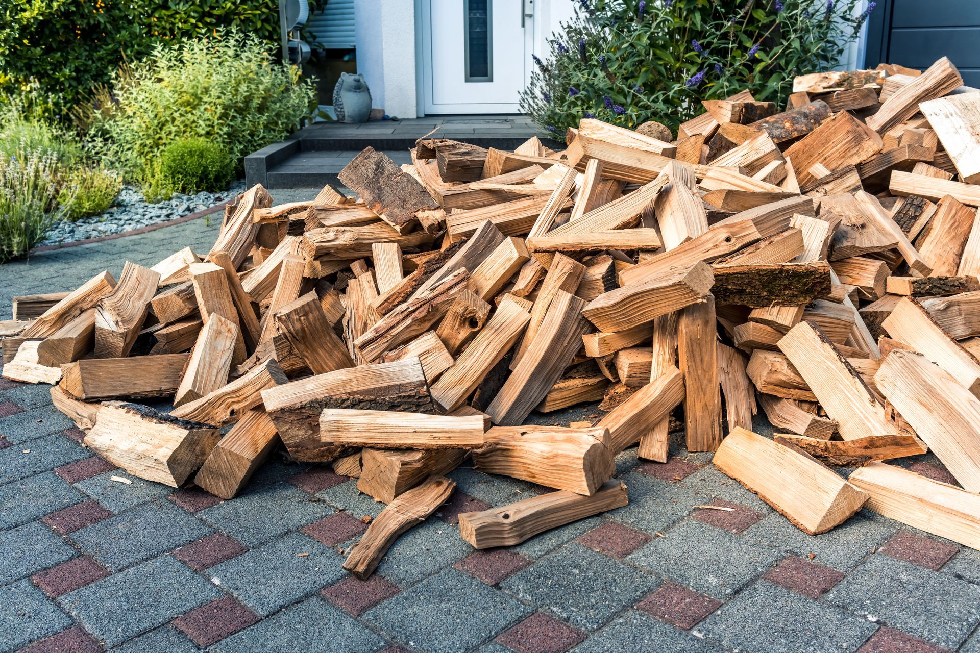 Pile of chopped firewood stacked on a paved driveway beside a house