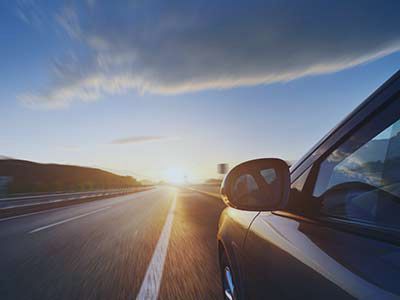 Car driving on a sunlit highway at sunset, with blue sky and road lines stretching ahead