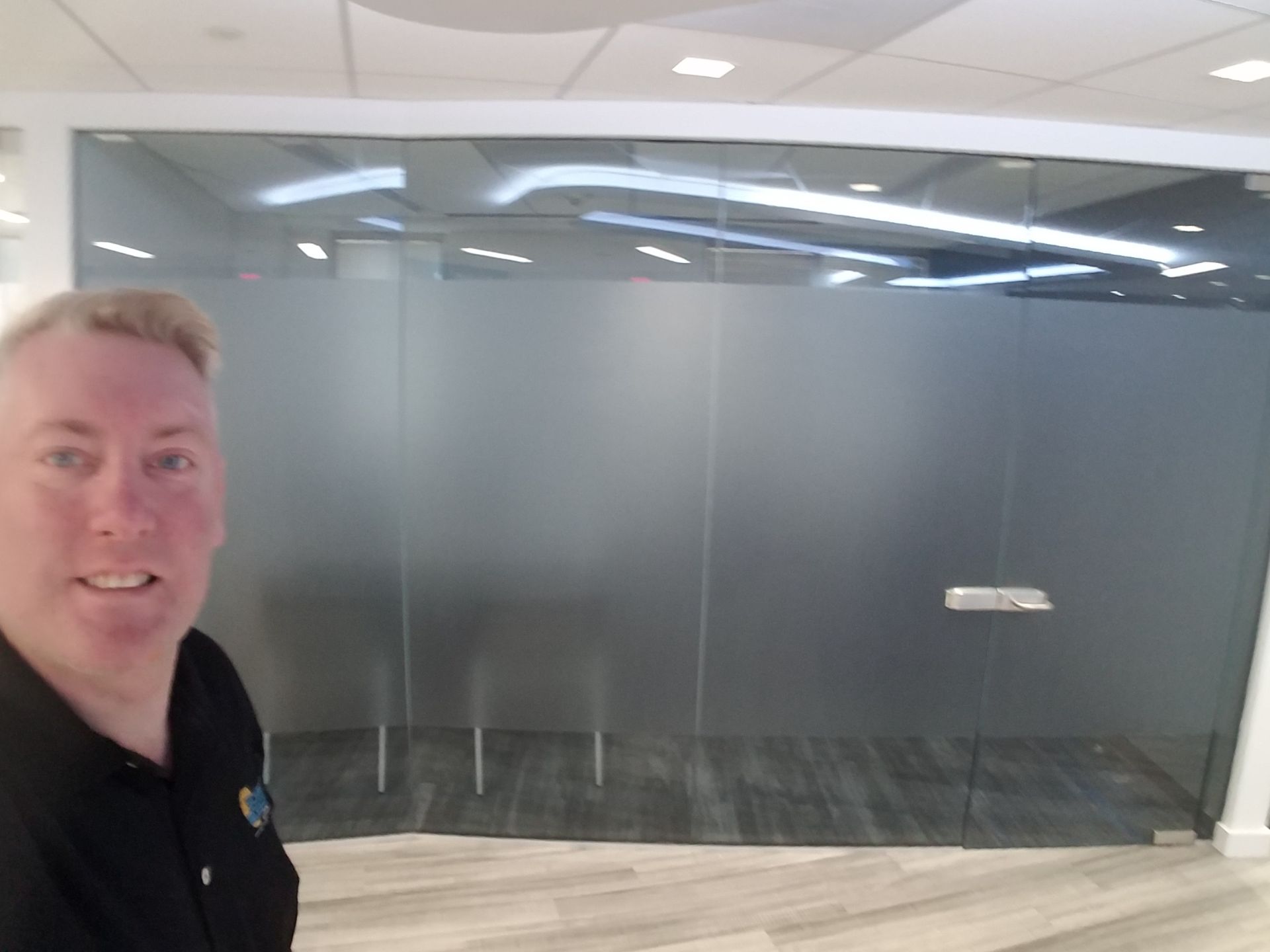 Man taking a selfie in front of frosted glass office doors in a bright hallway