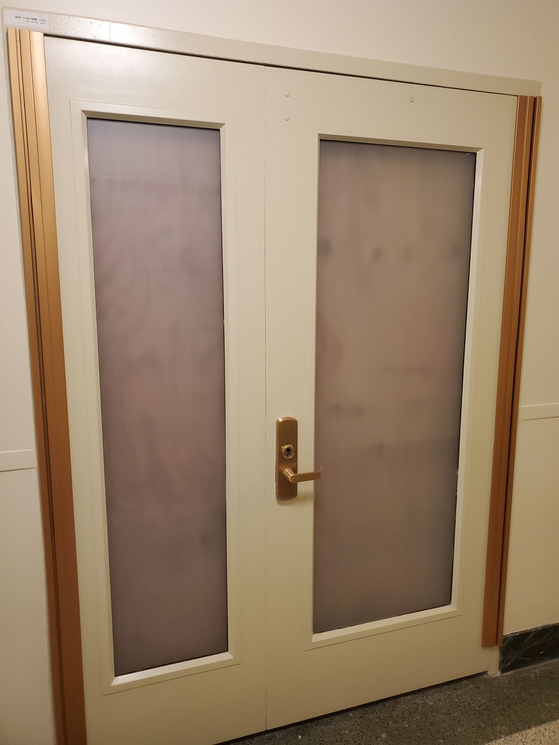 Cream-colored double door with two frosted glass panels and a brass handle in a hallway