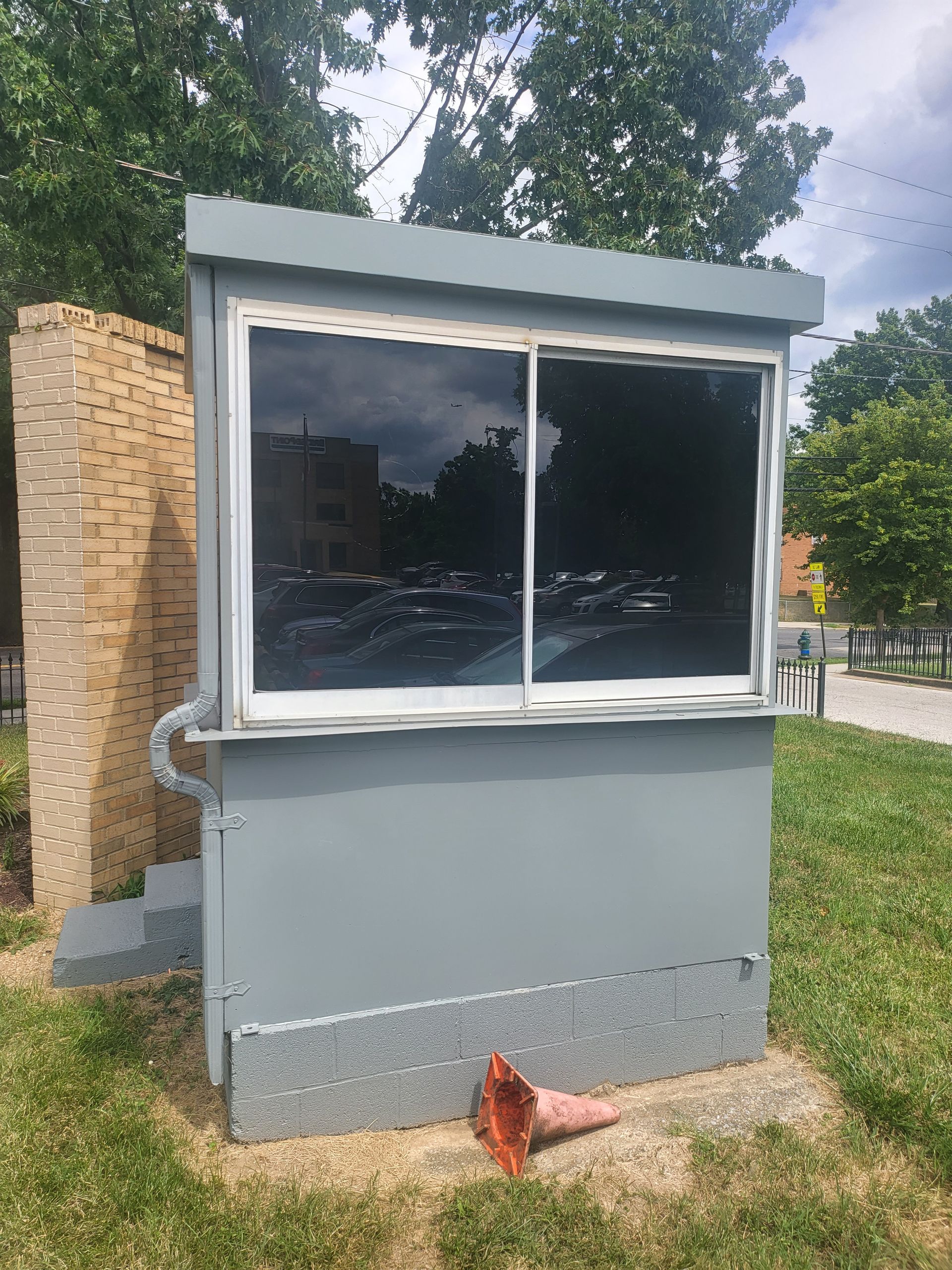 Small gray kiosk with large window beside a brick pillar in a grassy outdoor area