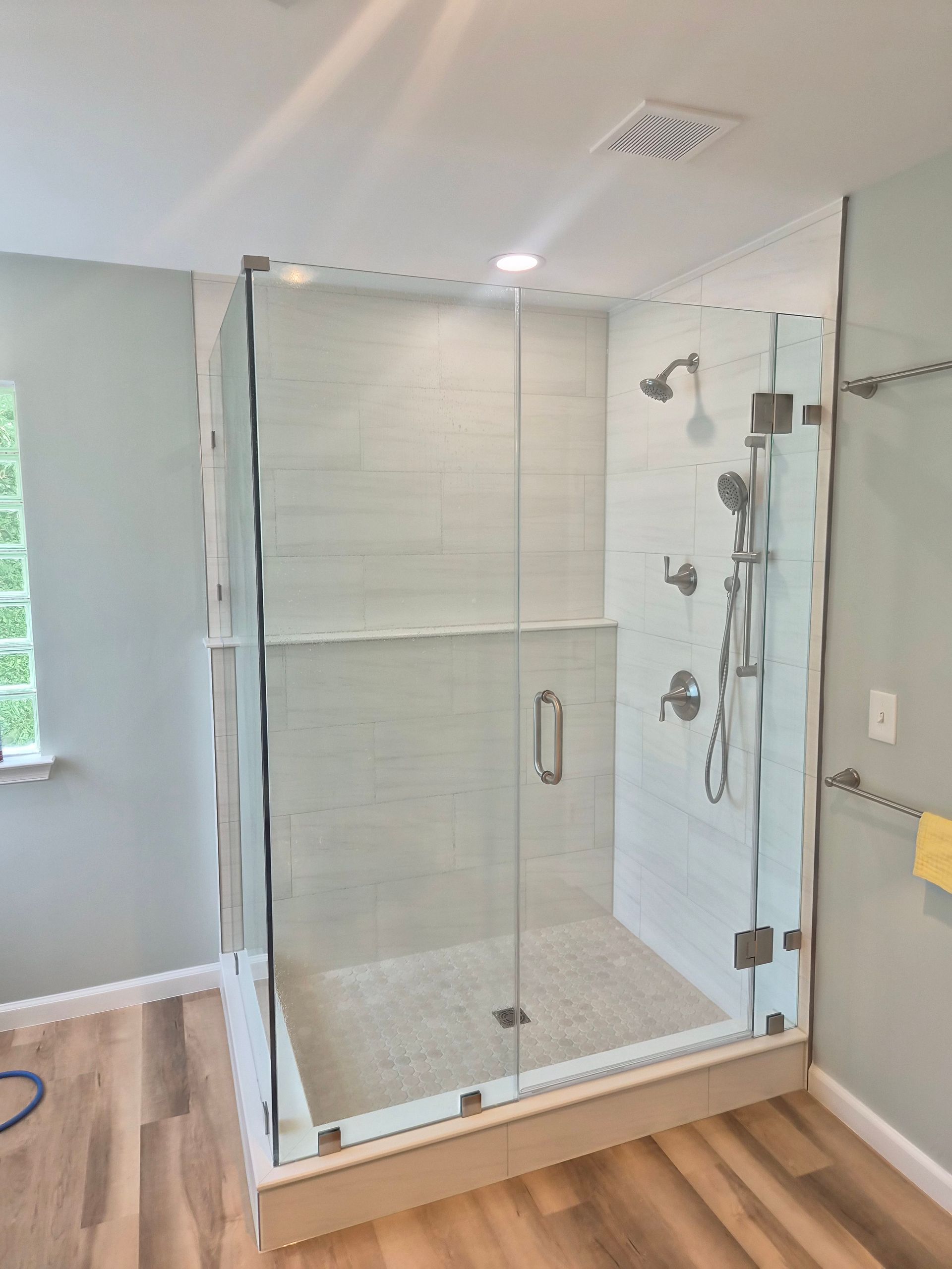 Modern bathroom with glass shower enclosure, white tile walls, and wood flooring