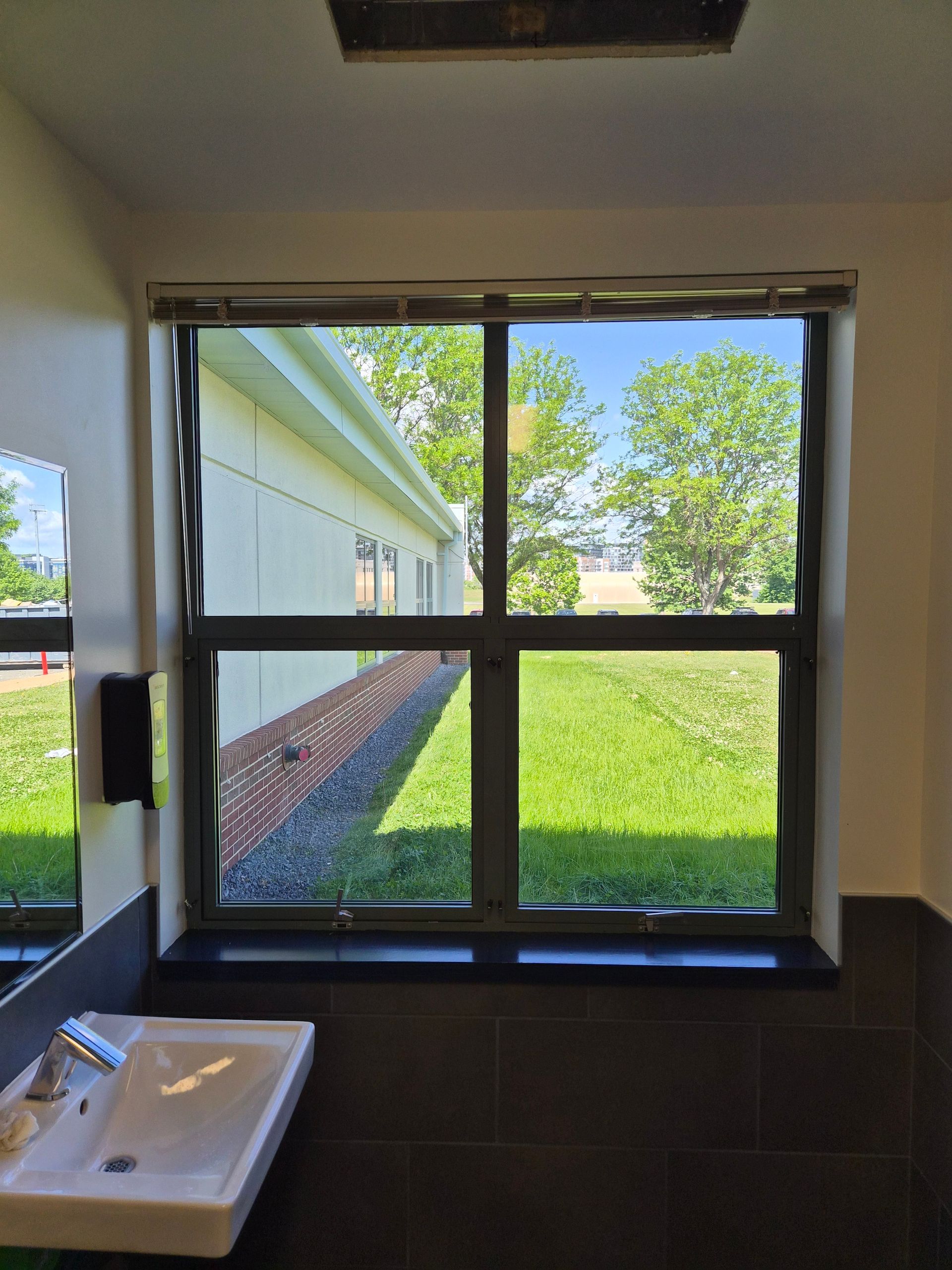 Small window in a restroom showing a grassy courtyard and building outside, with a sink below.