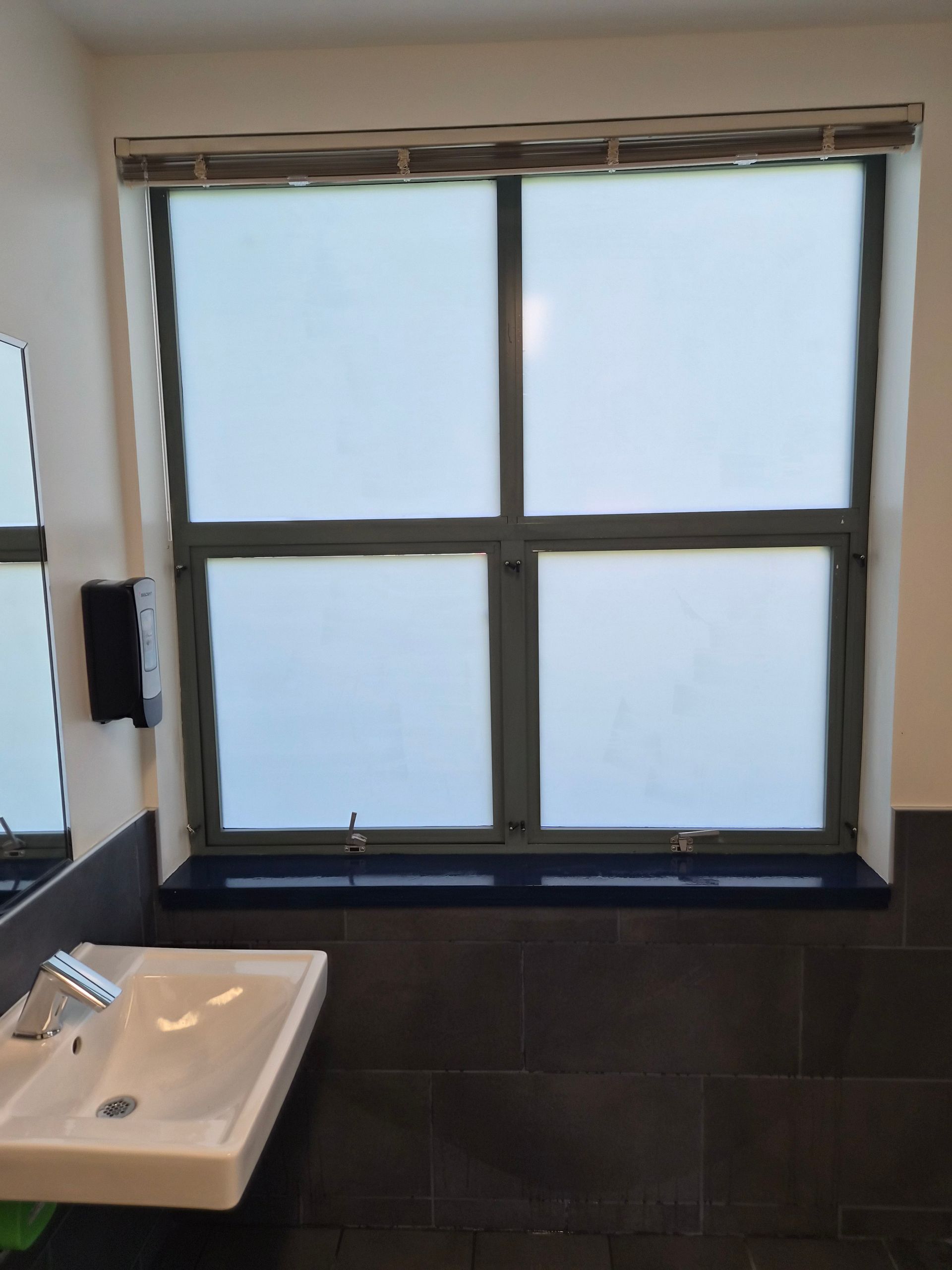 Small bathroom window above a dark countertop and white sink in a tiled room