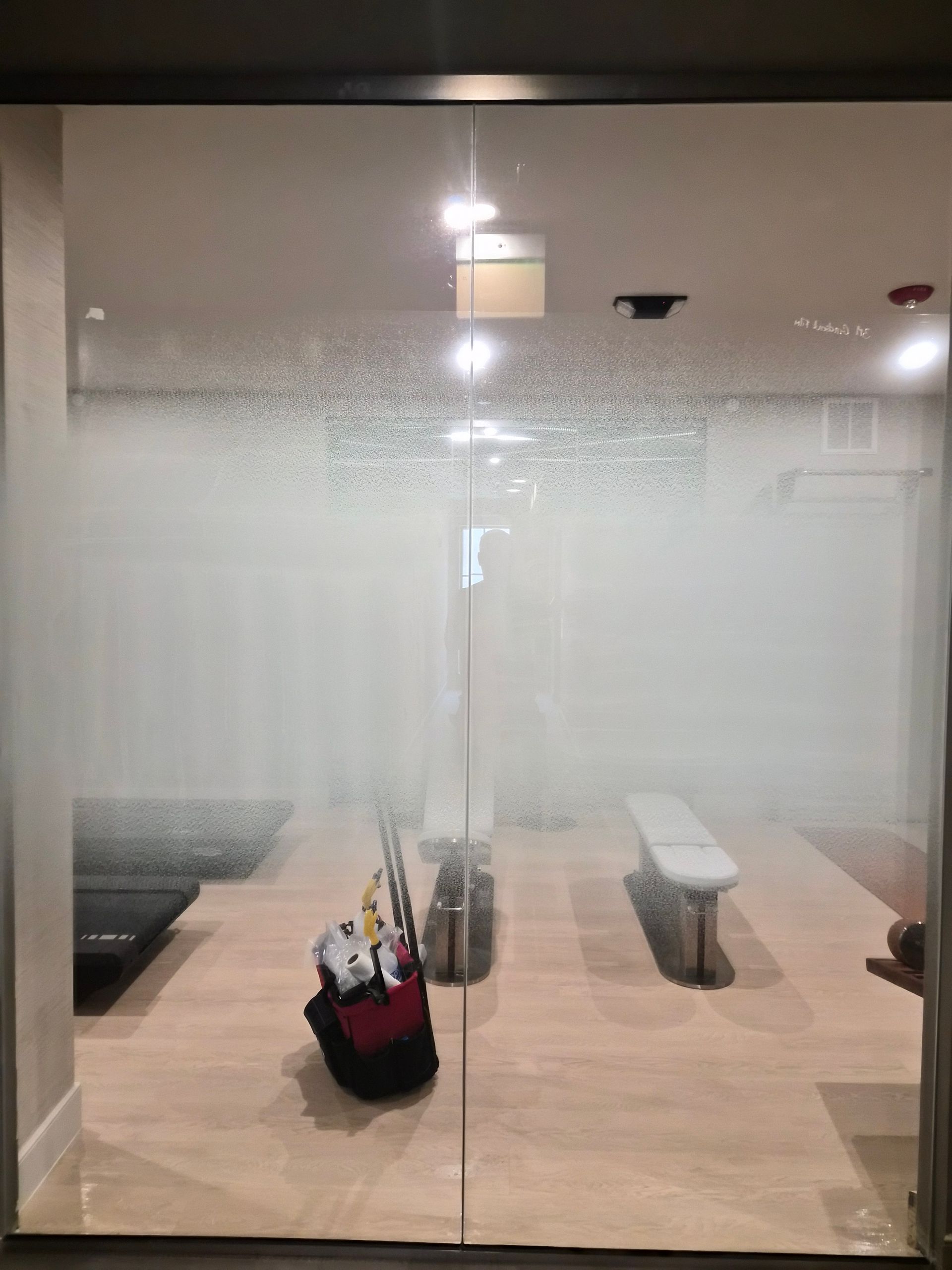 Frosted glass office with tables and chairs, viewed from outside through a partially obscured door.