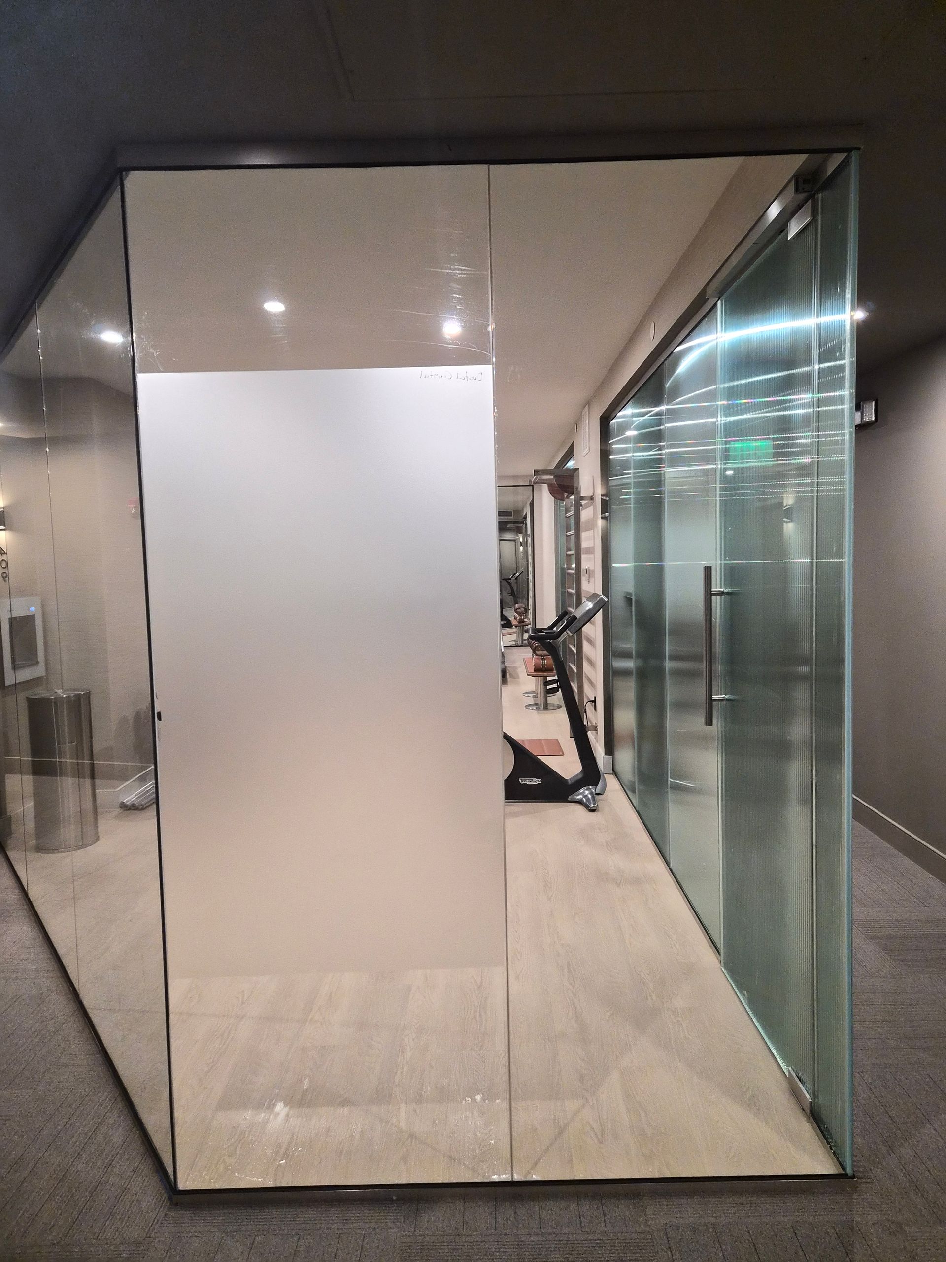 Mirrored wall in a hallway with glass doors and a seated person reflected in the center.