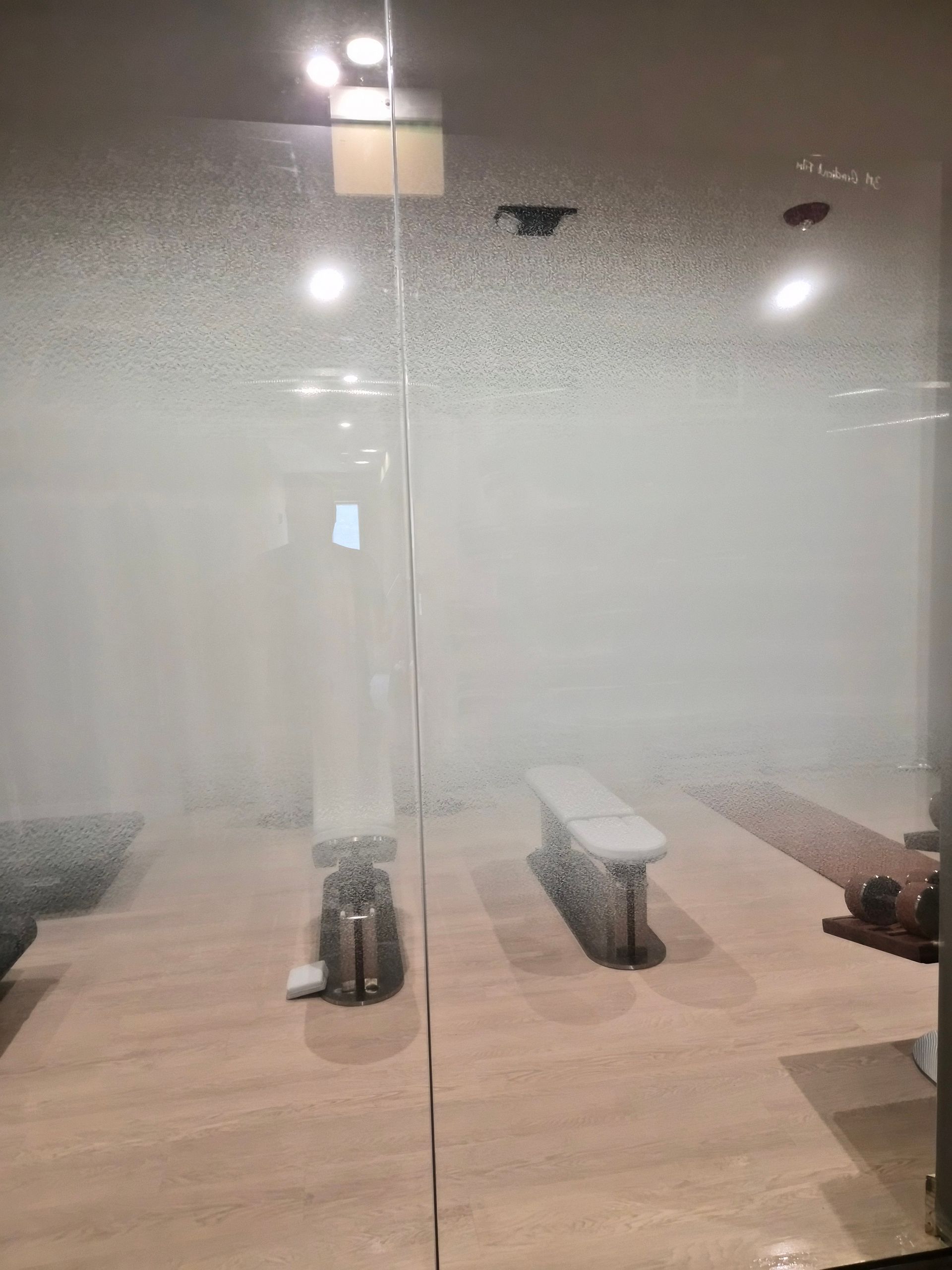 Frosted glass sauna interior with wooden benches and warm ceiling lights