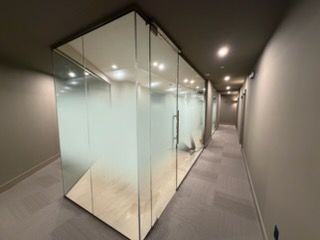 Modern hallway with glass office pods, gray carpet, and ceiling lights