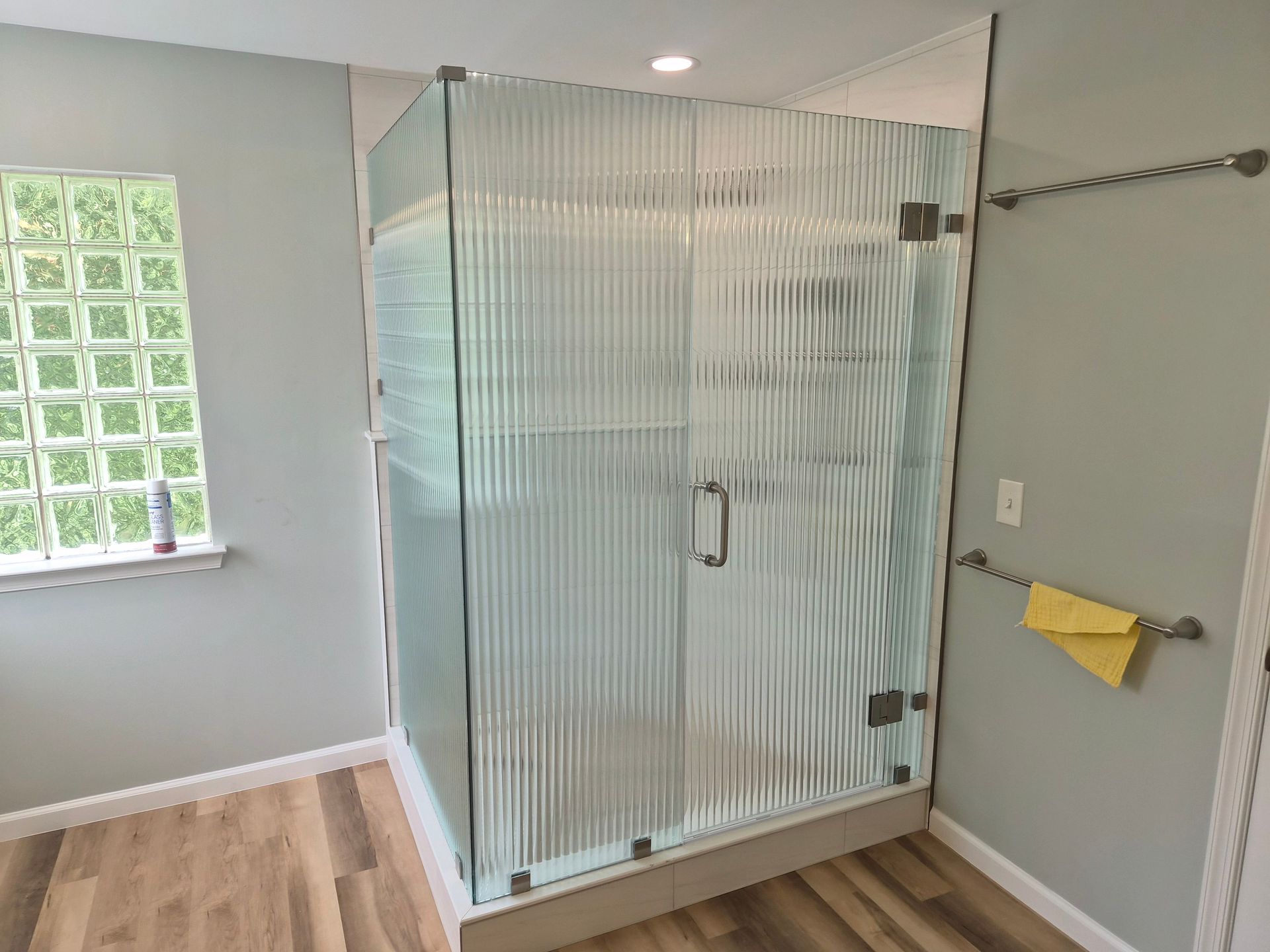 Modern bathroom with a glass shower enclosure, gray walls, and wood-look flooring