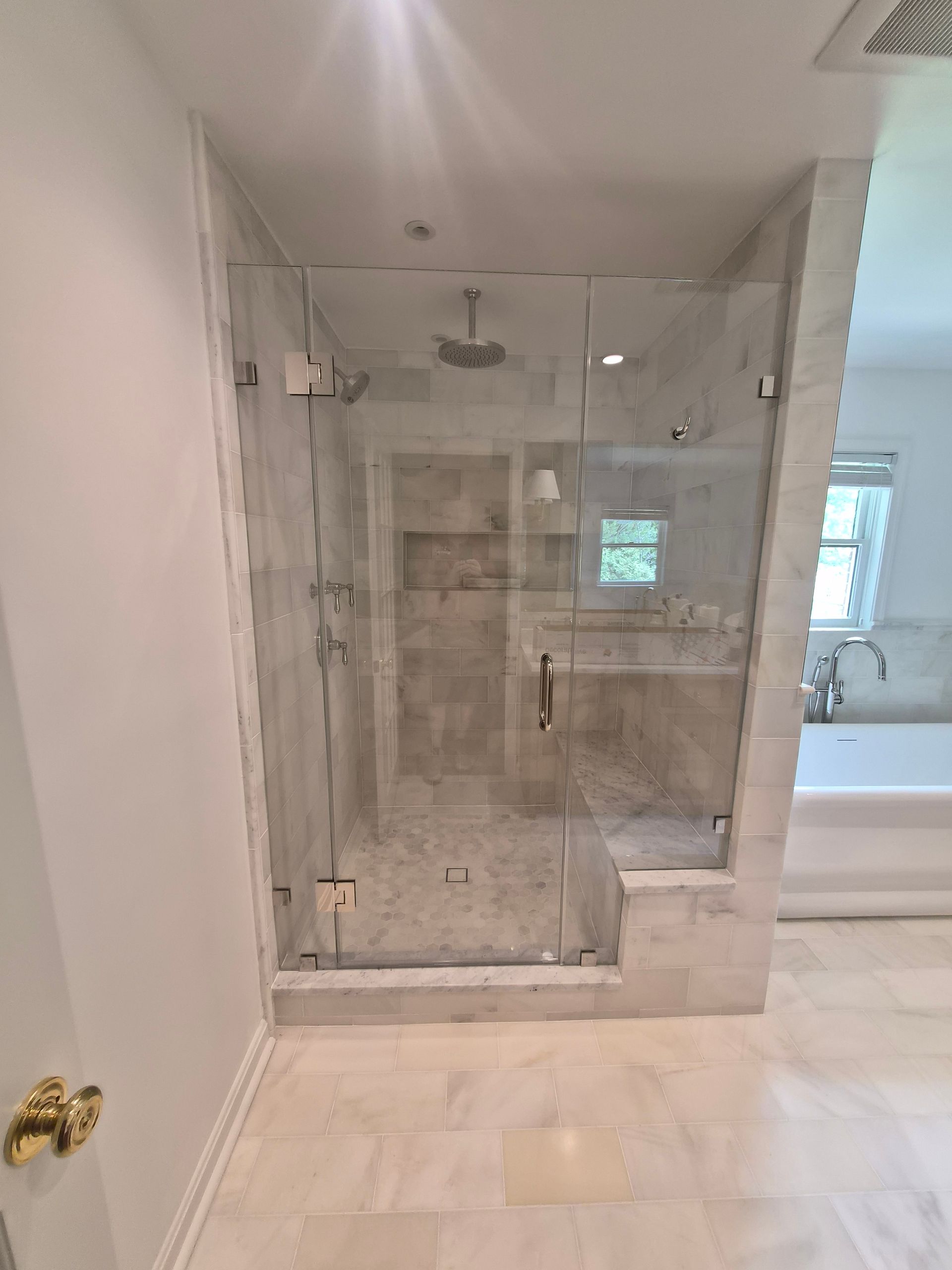 Glass-enclosed tiled shower in a modern bathroom with marble-look walls and floor