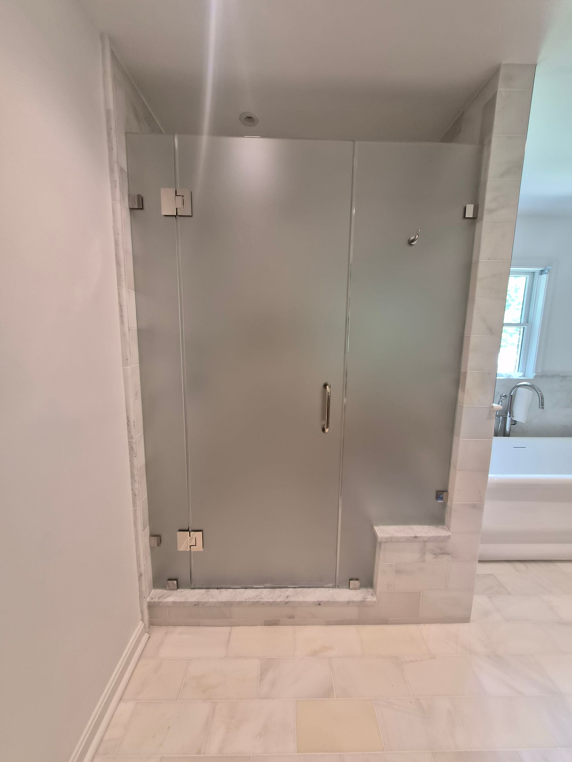 Small bathroom with frosted glass shower doors, tiled floor, and a sink visible through an opening.