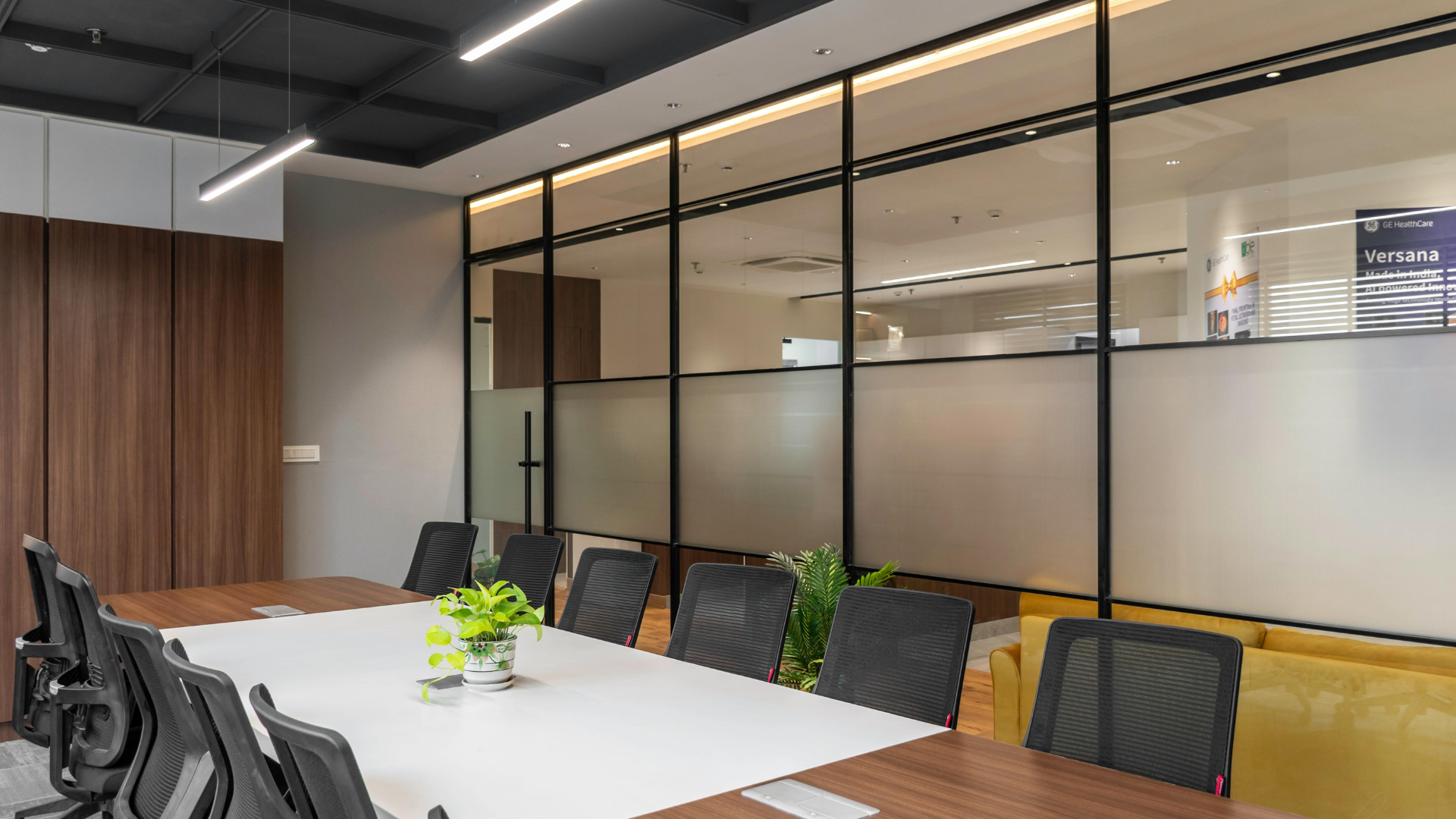Modern conference room with long table, black chairs, glass walls, and wood-paneled accents