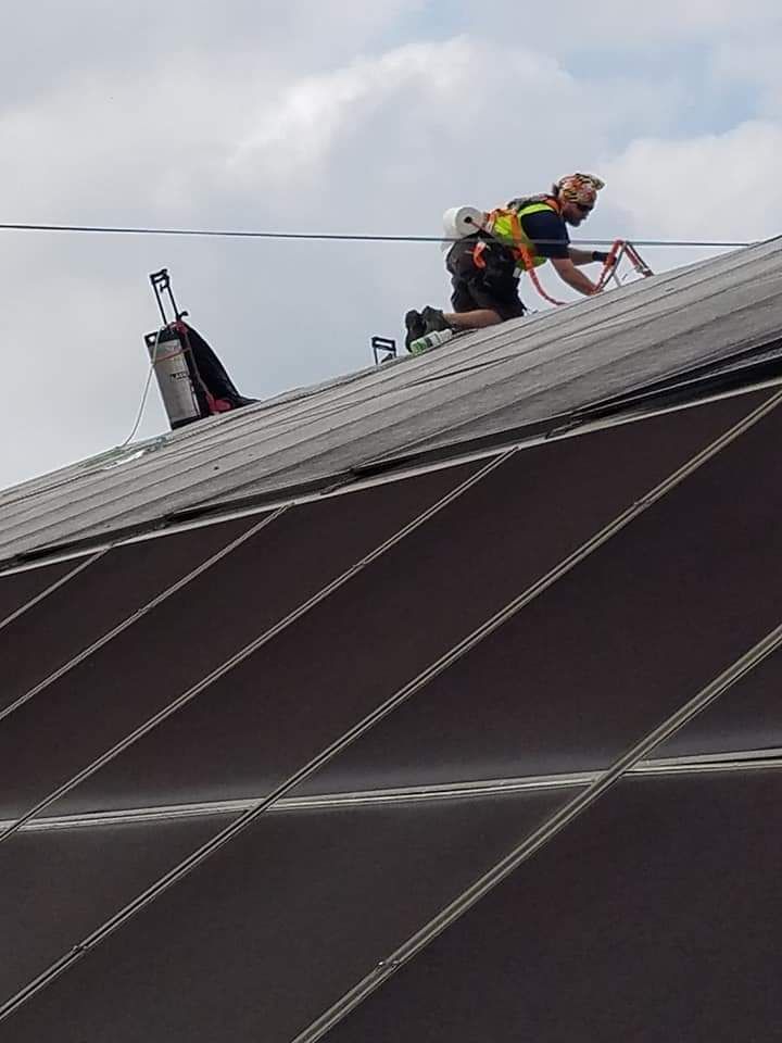 Worker on a steep rooftop installing or repairing equipment with cables under a cloudy sky