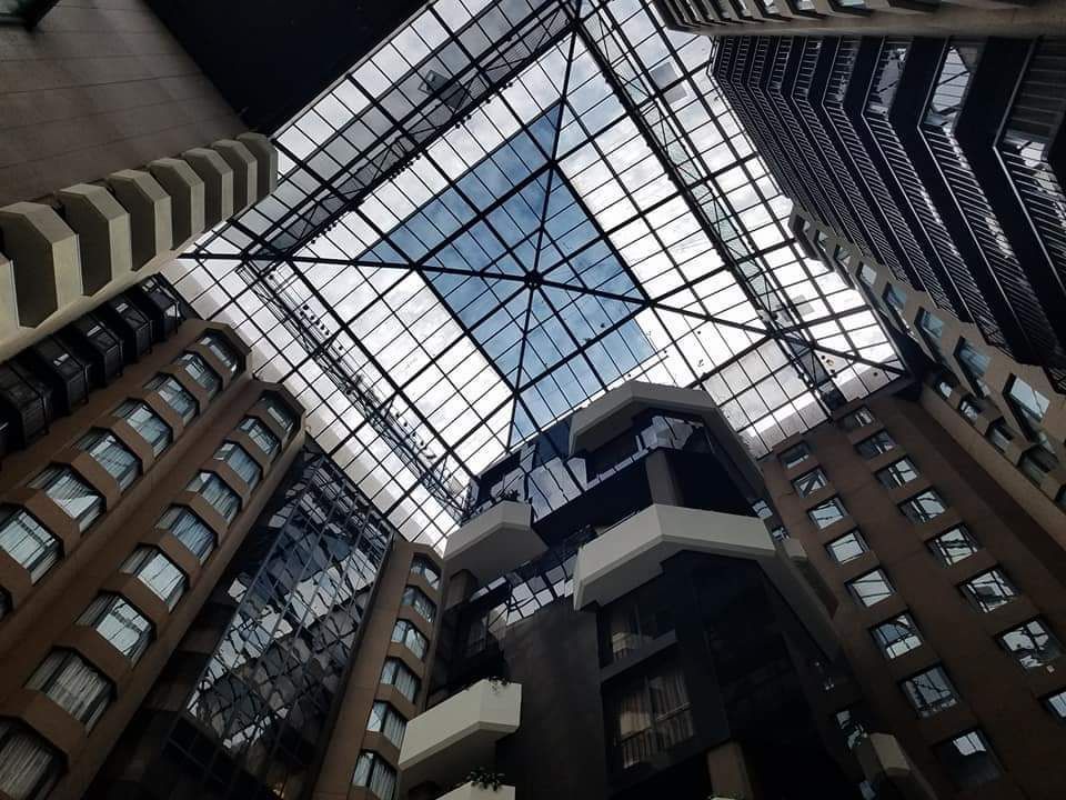 Looking up inside a glass-roofed atrium surrounded by tall brick apartment buildings