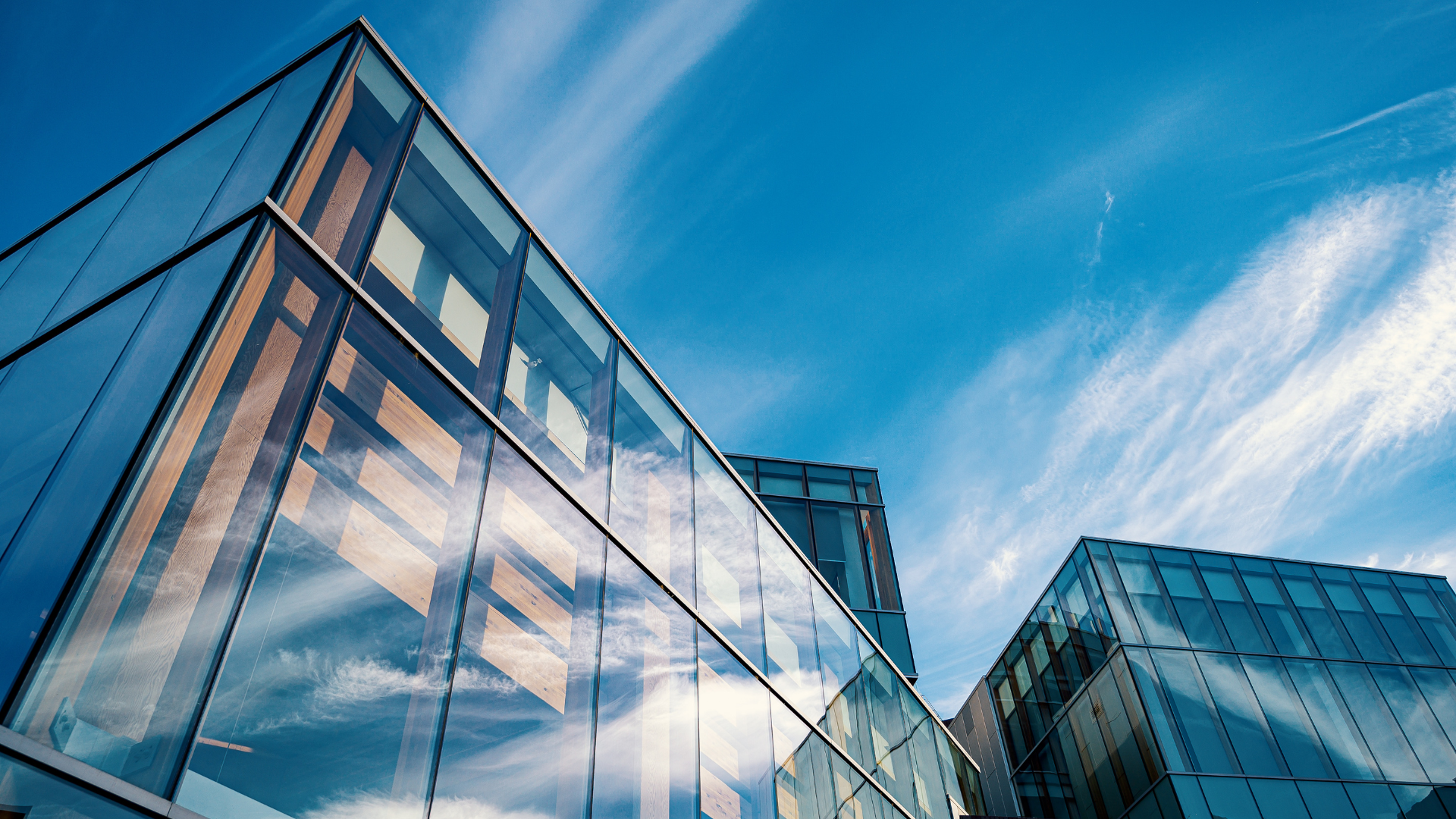 Modern glass office buildings reflecting a blue sky with wispy clouds