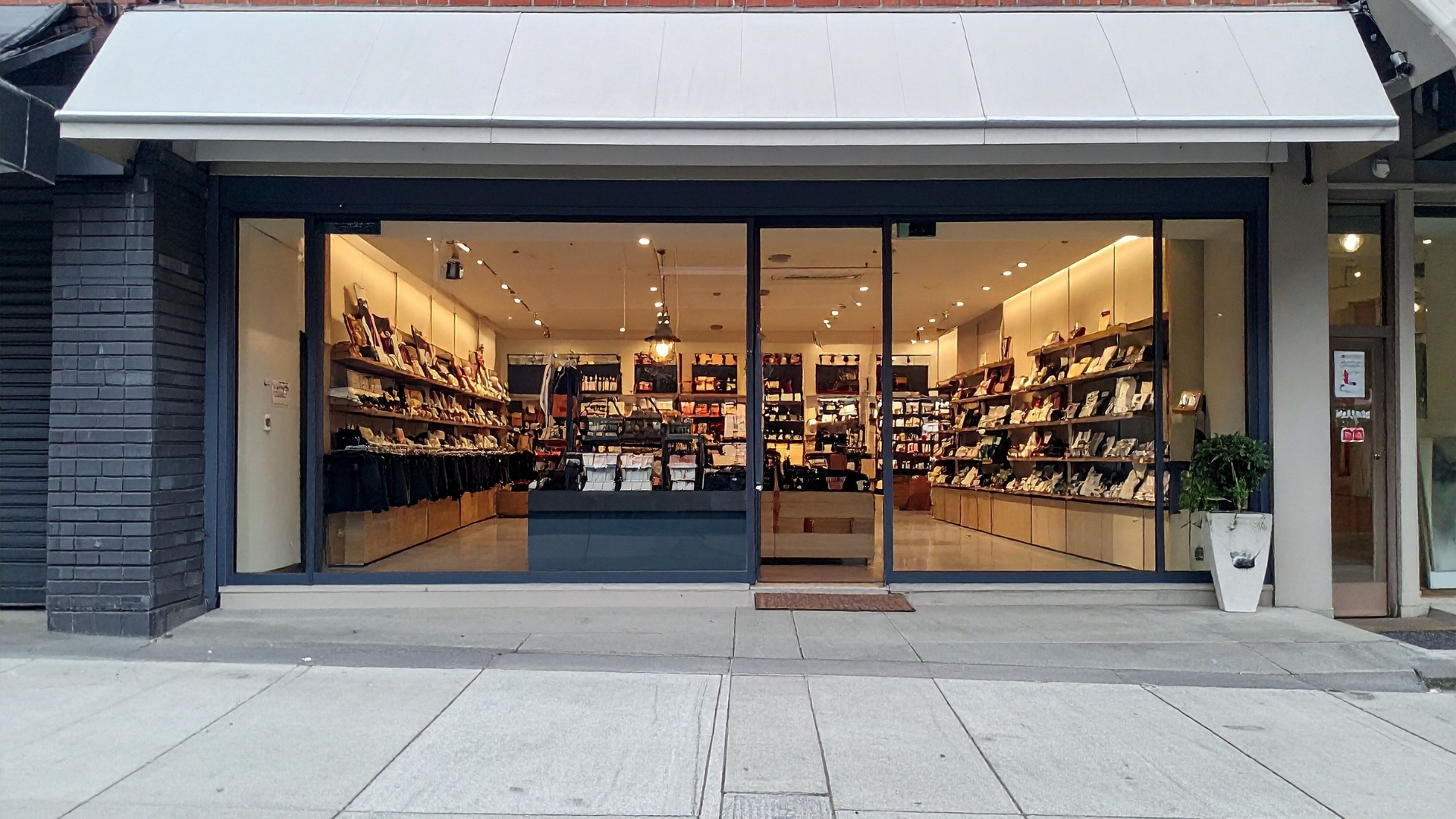 Wide storefront bakery or café with warm-lit interior and pastry displays behind large glass windows.