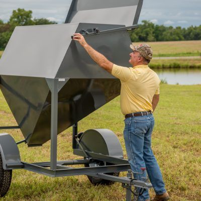 gray feed trailer with adult man grabbing handle to open lid