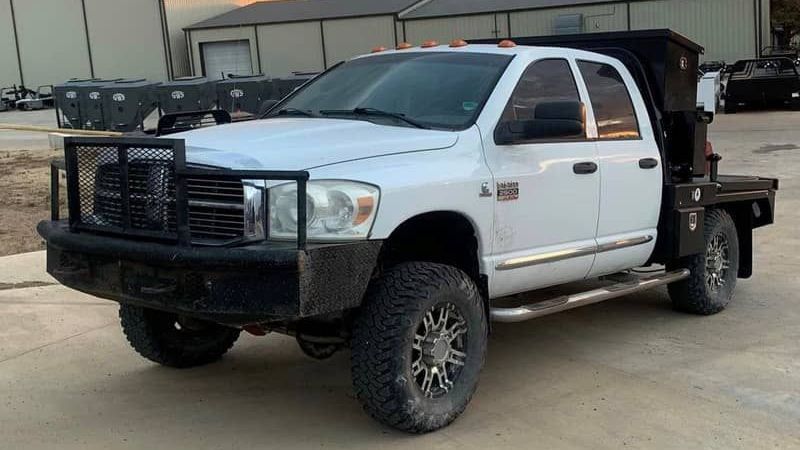 a white ram truck with a flat bed cube feeder is parked in a parking lot .