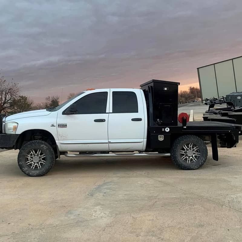 a white ram truck with a crownline flat bed is parked in a parking lot .