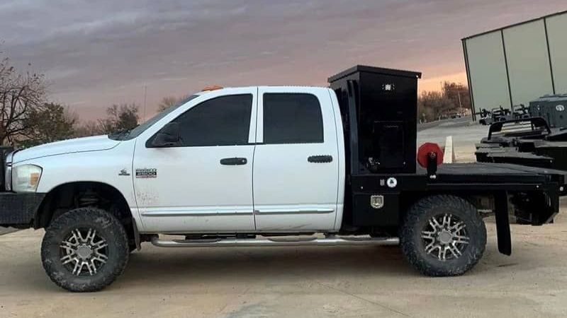 a white ram truck with a flat bed with cake feeder is parked in a parking lot .
