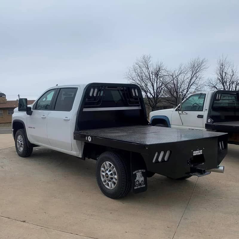 a white chevy truck with a black flat bed is parked next to another truck .